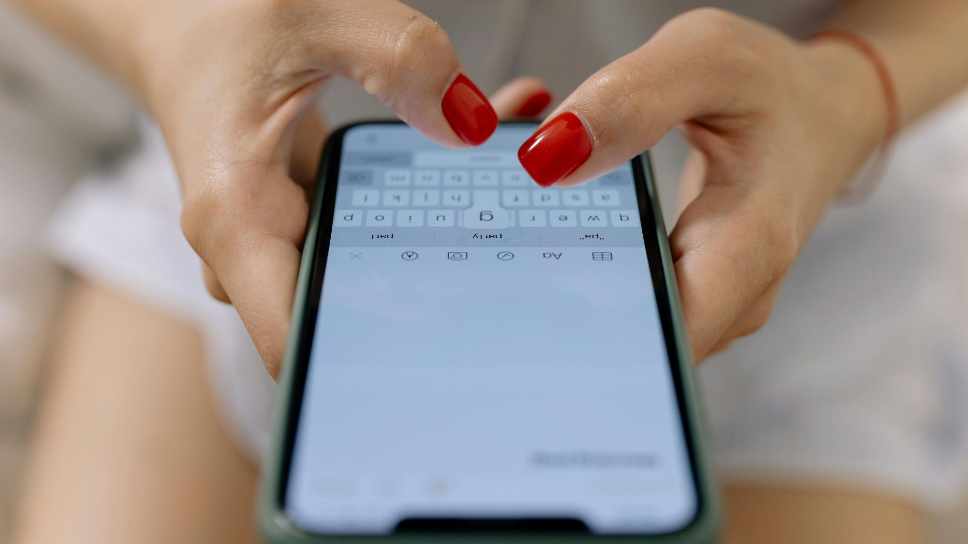 Close-up image of hands with red nails typing on a smartphone screen, showcasing modern technology.