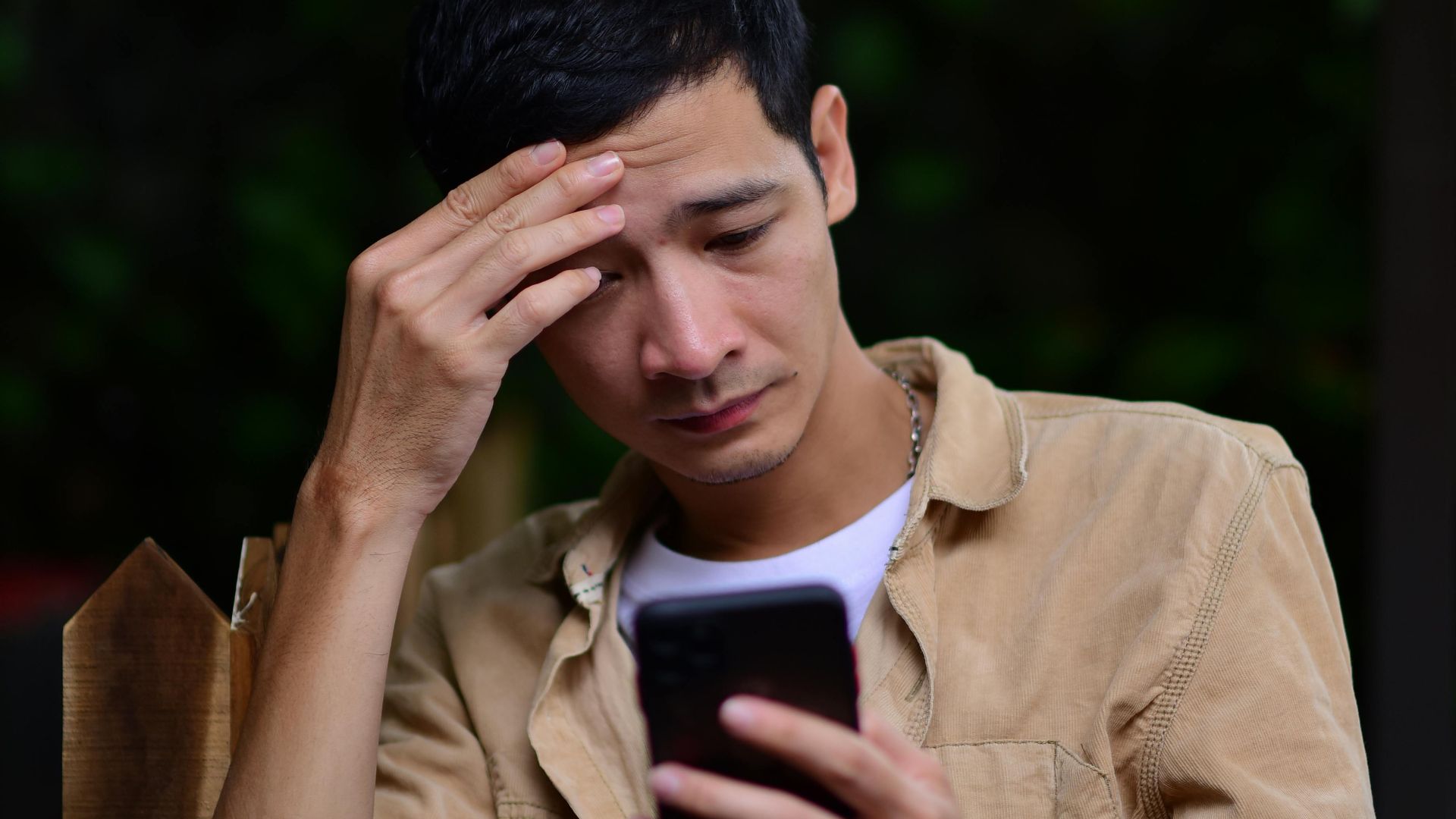 A young man looks stressed while checking his smartphone outdoors, possibly receiving bad news.
