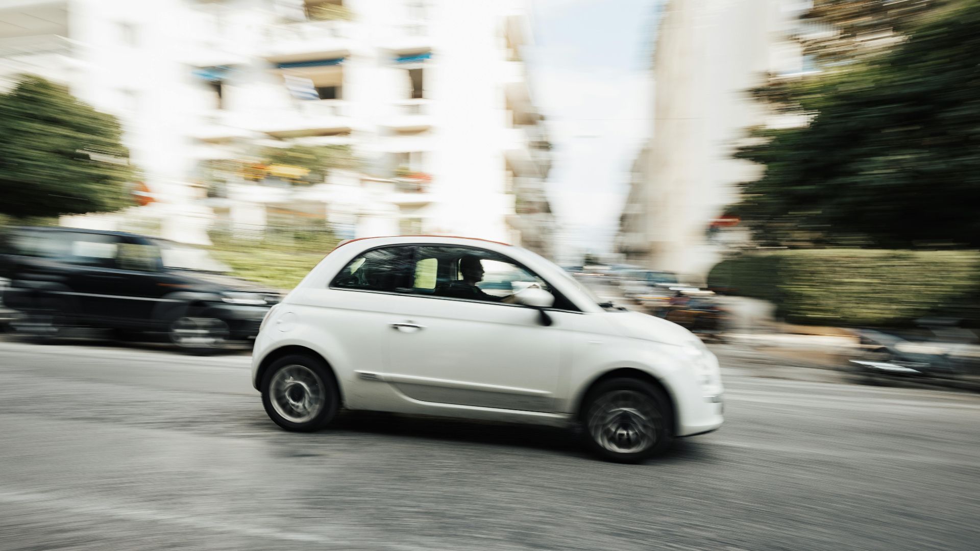 Dynamic capture of a compact white car speeding through a city street with motion blur effect.