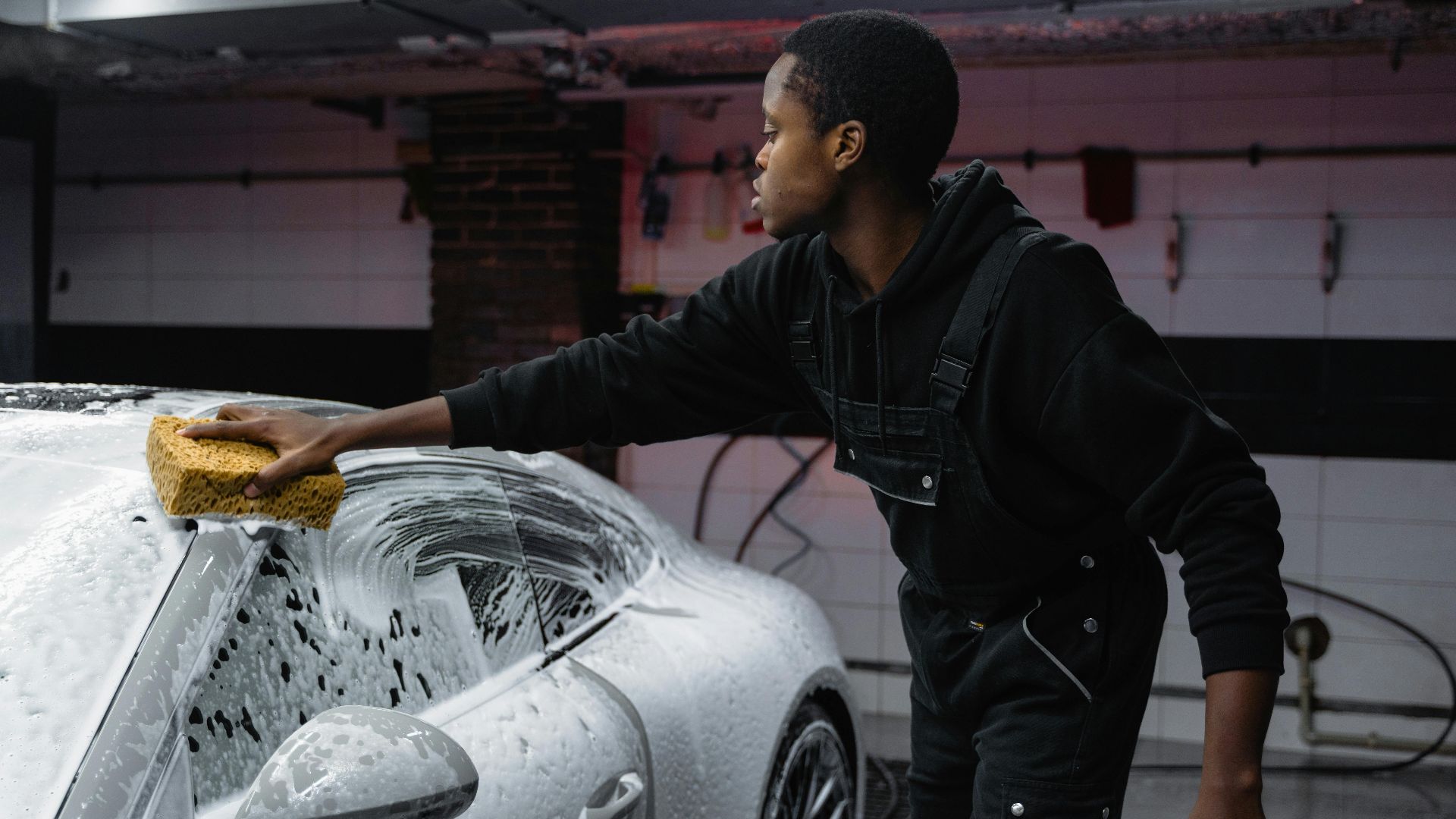 A person washing a car with a sponge, deep cleaning in a garage setting.
