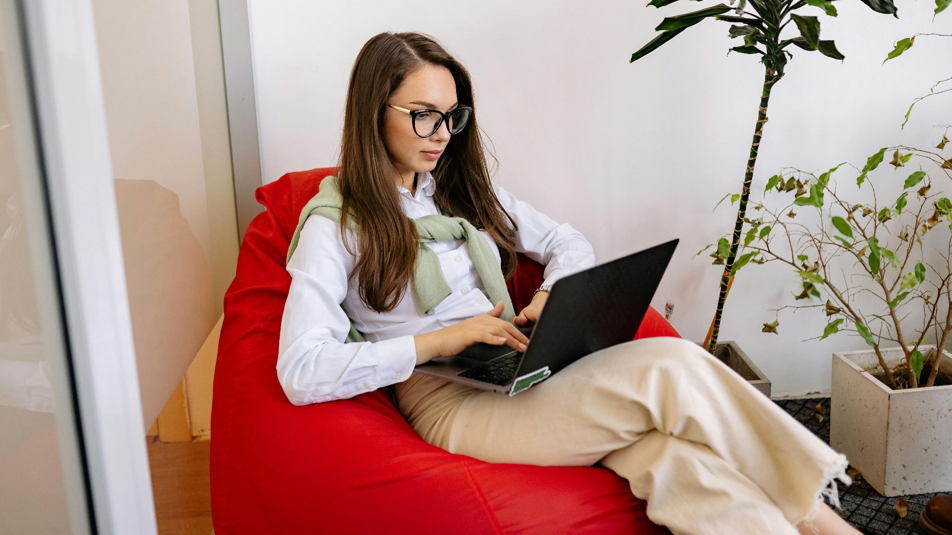 Woman working on laptop while relaxing in a bean bag in modern indoor setting.
