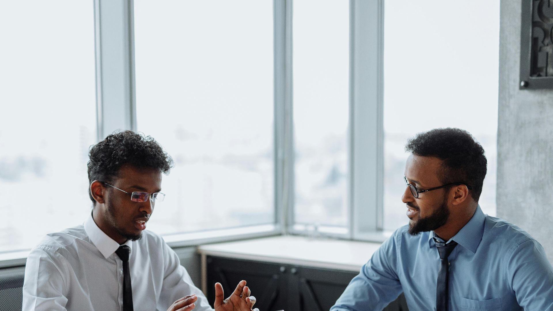 Two African American professionals discussing a project in an office with laptops.