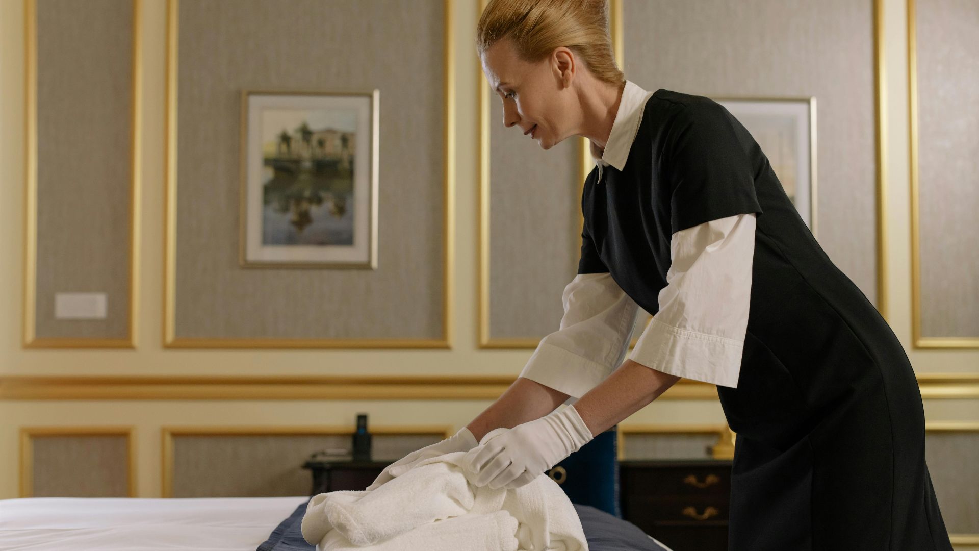 A housekeeper neatly folds sheets on a luxury hotel bed, emphasizing professional service.