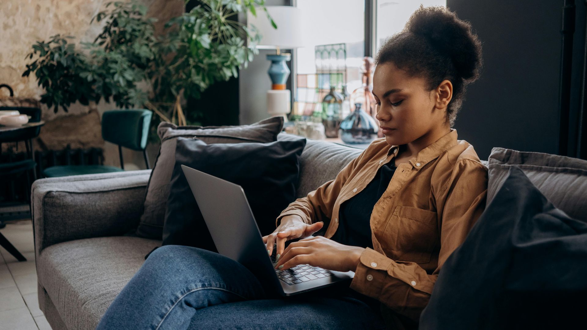 Young woman working from home on a laptop in a cozy living room setting.