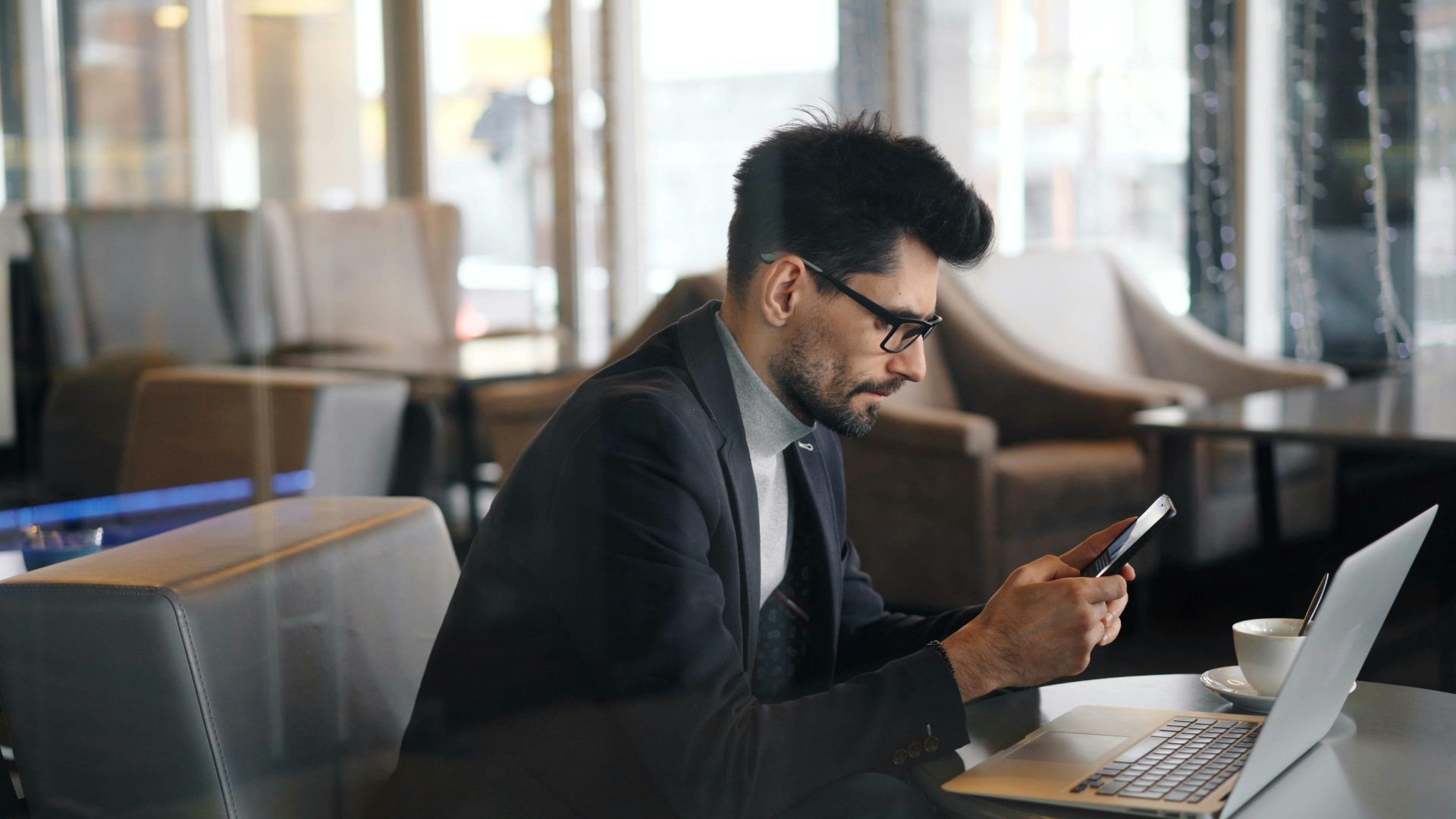 Confident businessman using smartphone in a modern café setting.