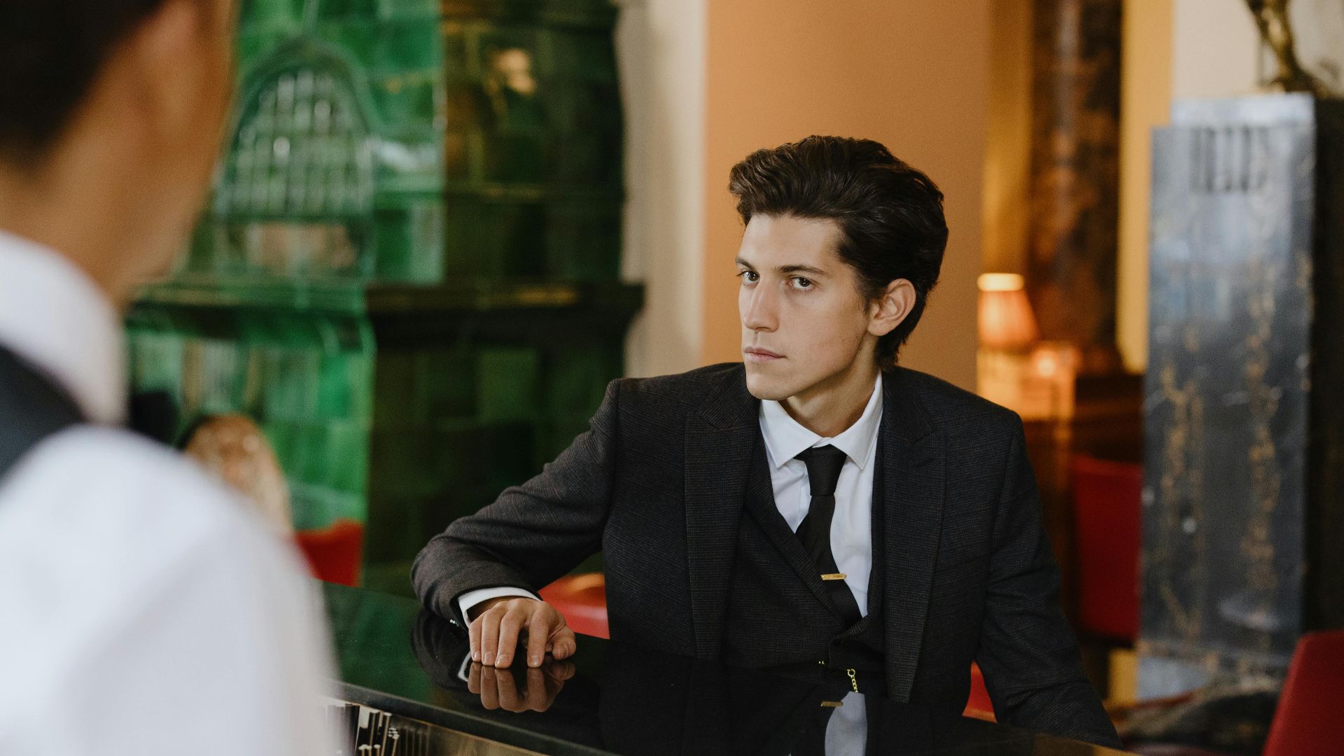 Sophisticated man in a suit sitting at a vintage bar counter indoors, exuding elegance and style.