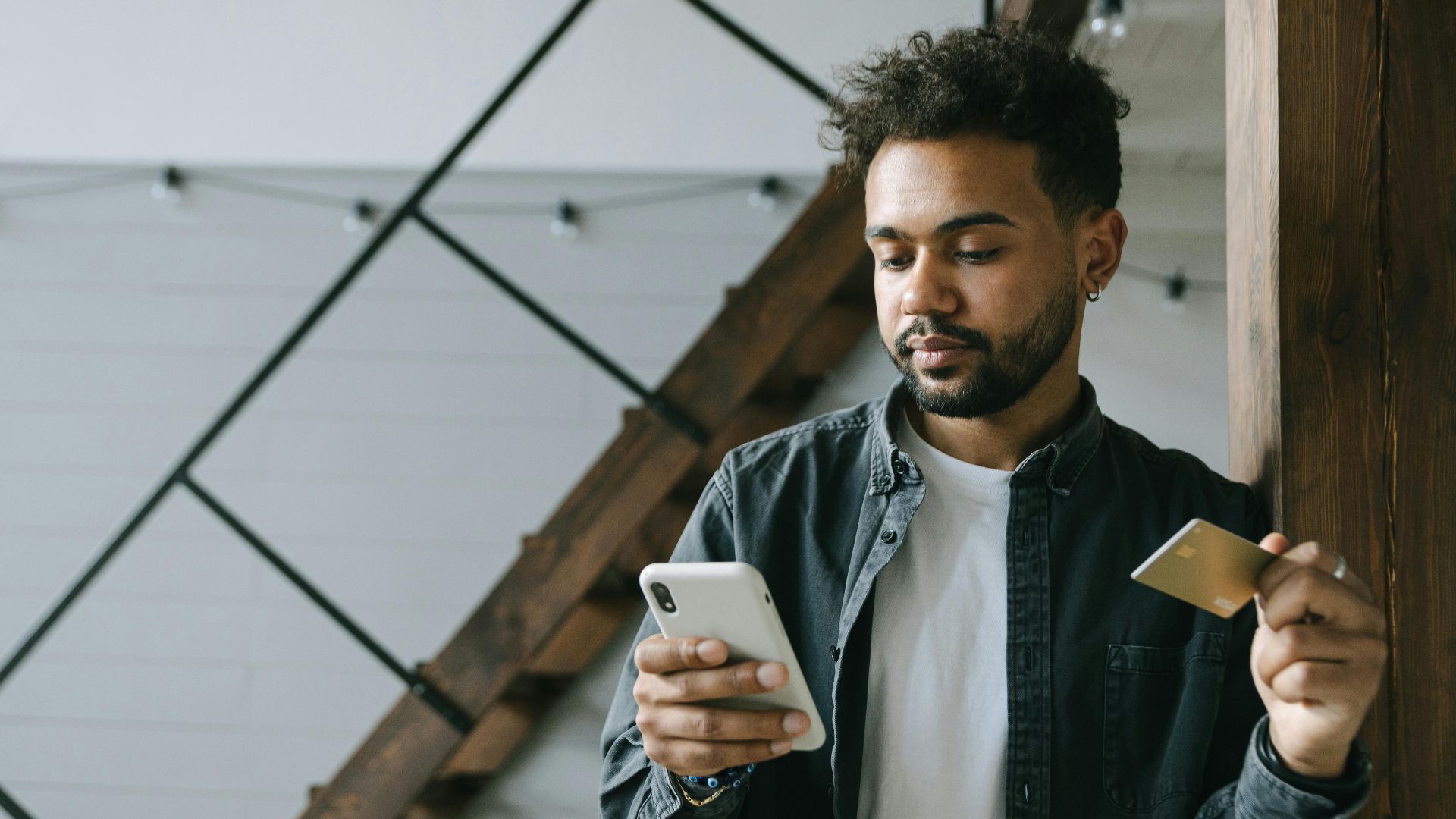 A young man using a smartphone and credit card for online shopping indoors.