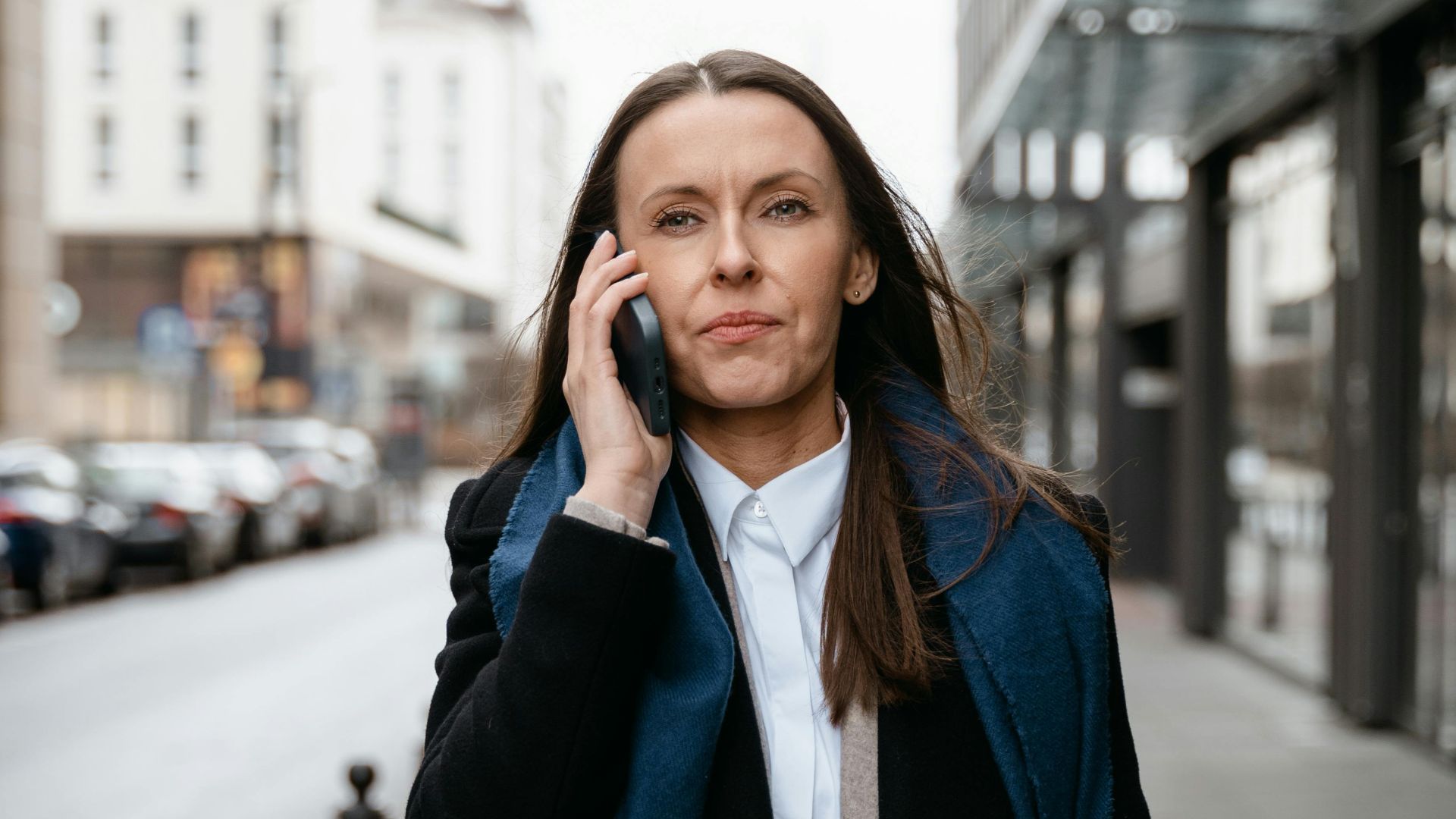 Professional woman walking in urban setting, engaged in cellphone conversation.