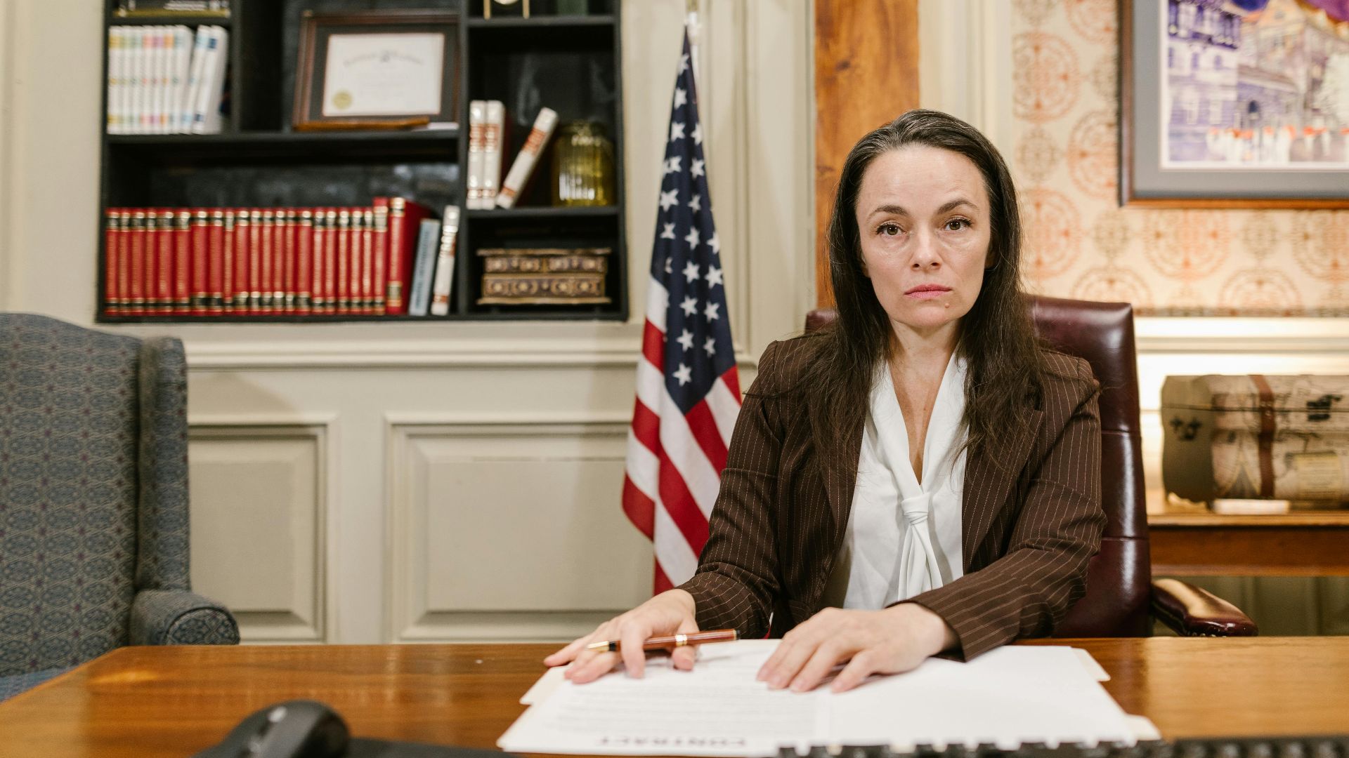 Confident female lawyer at her desk in a law office with legal books and the American flag.