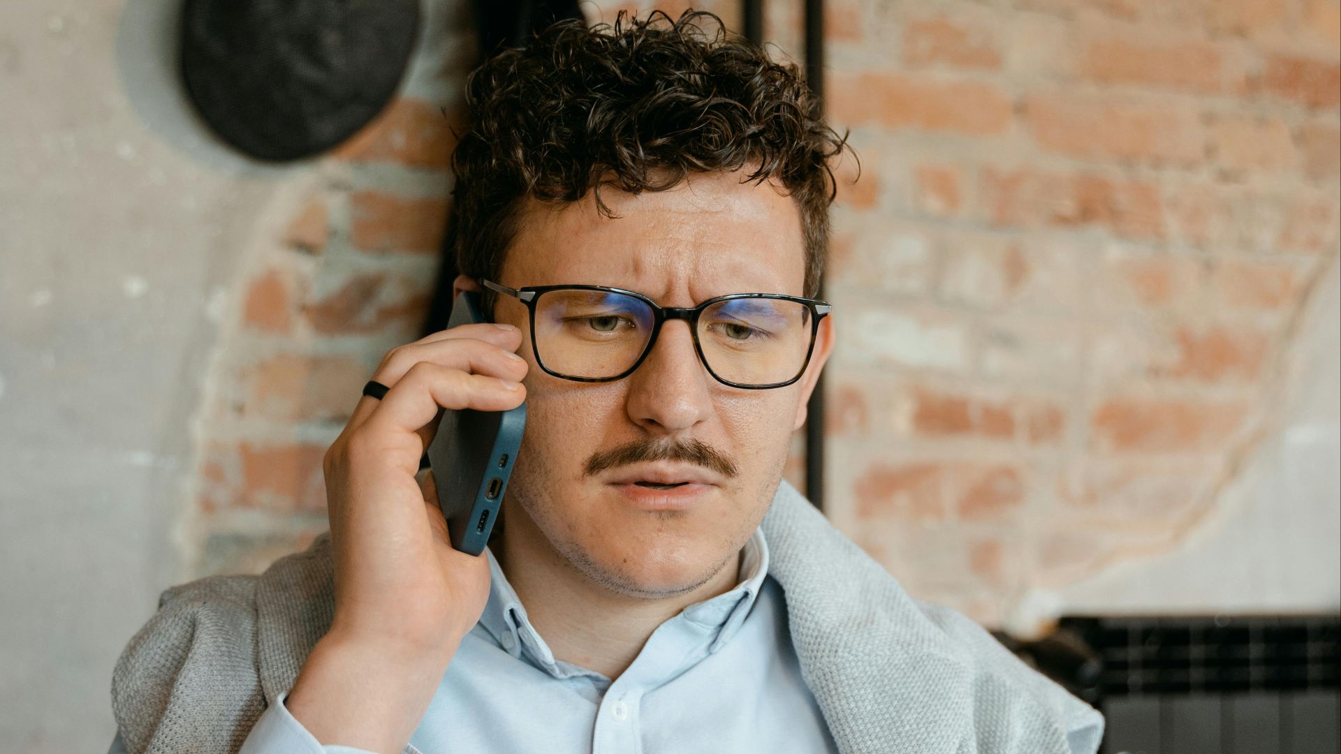 Young man in a casual indoor setting, making a phone call while wearing glasses.
