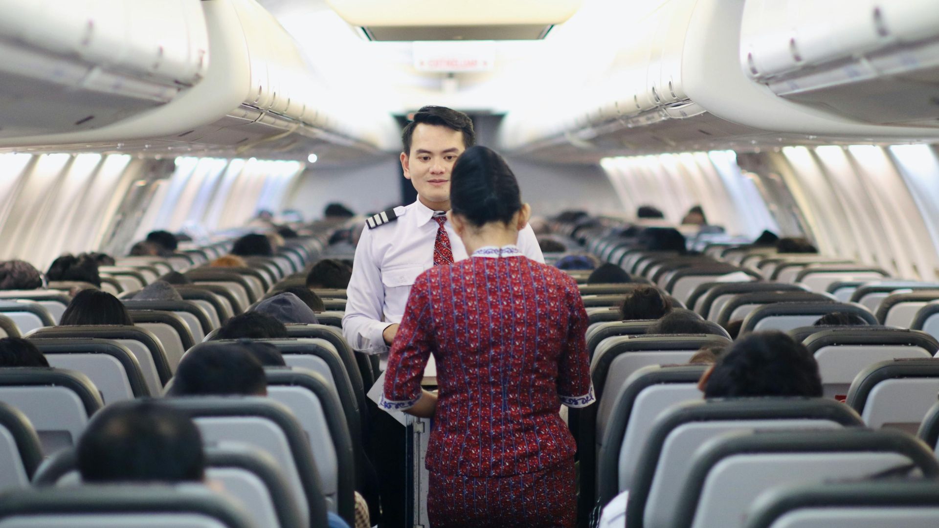 Flight attendants serving passengers inside an airplane cabin during a flight.