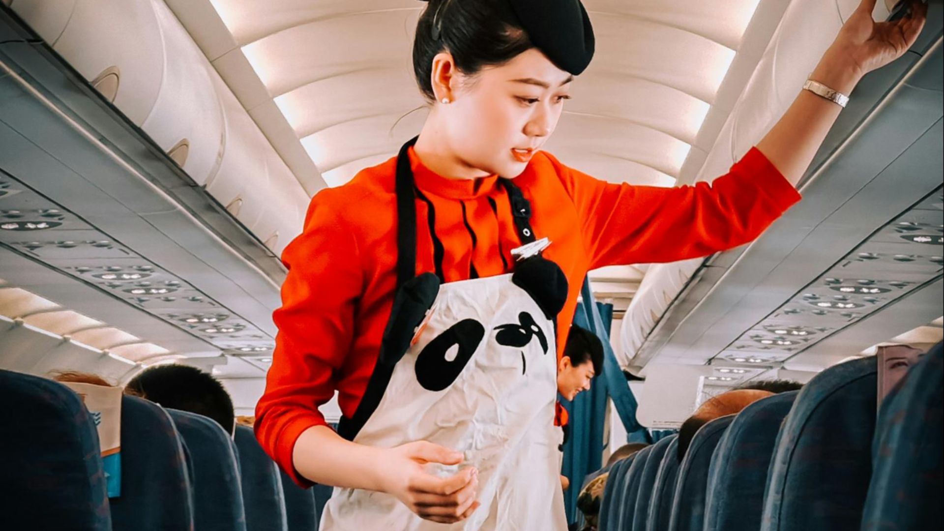Flight attendant in panda-themed apron assisting passengers during flight.