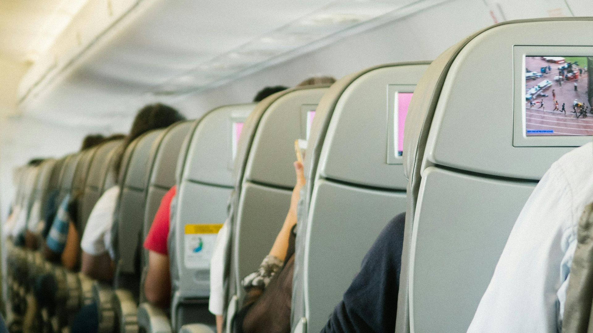 View of passengers seated in an airplane cabin, focusing on seatbacks and screens.