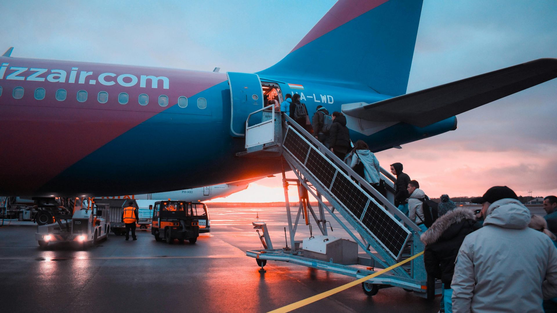 Passengers boarding an airplane at sunset with a vivid sky in the background, capturing a travel moment.