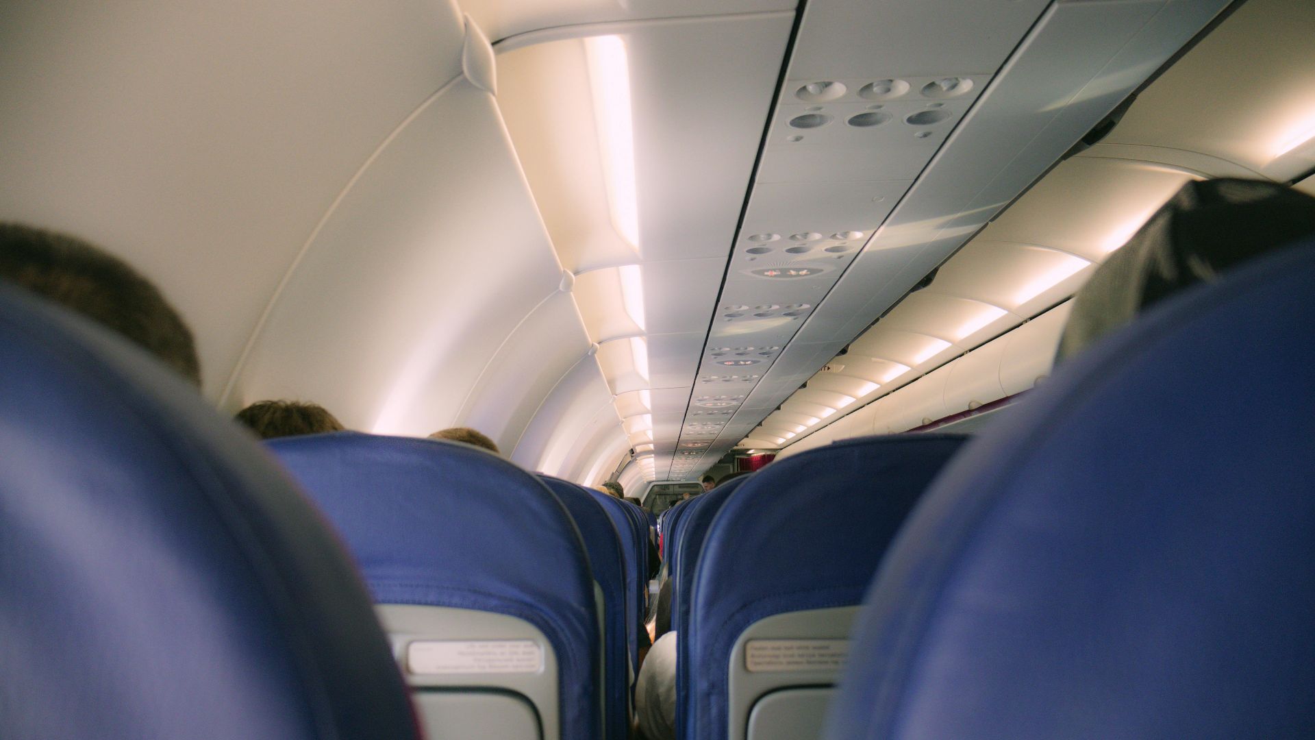 A view of a modern airplane cabin showing rows of blue seats and overhead compartments.