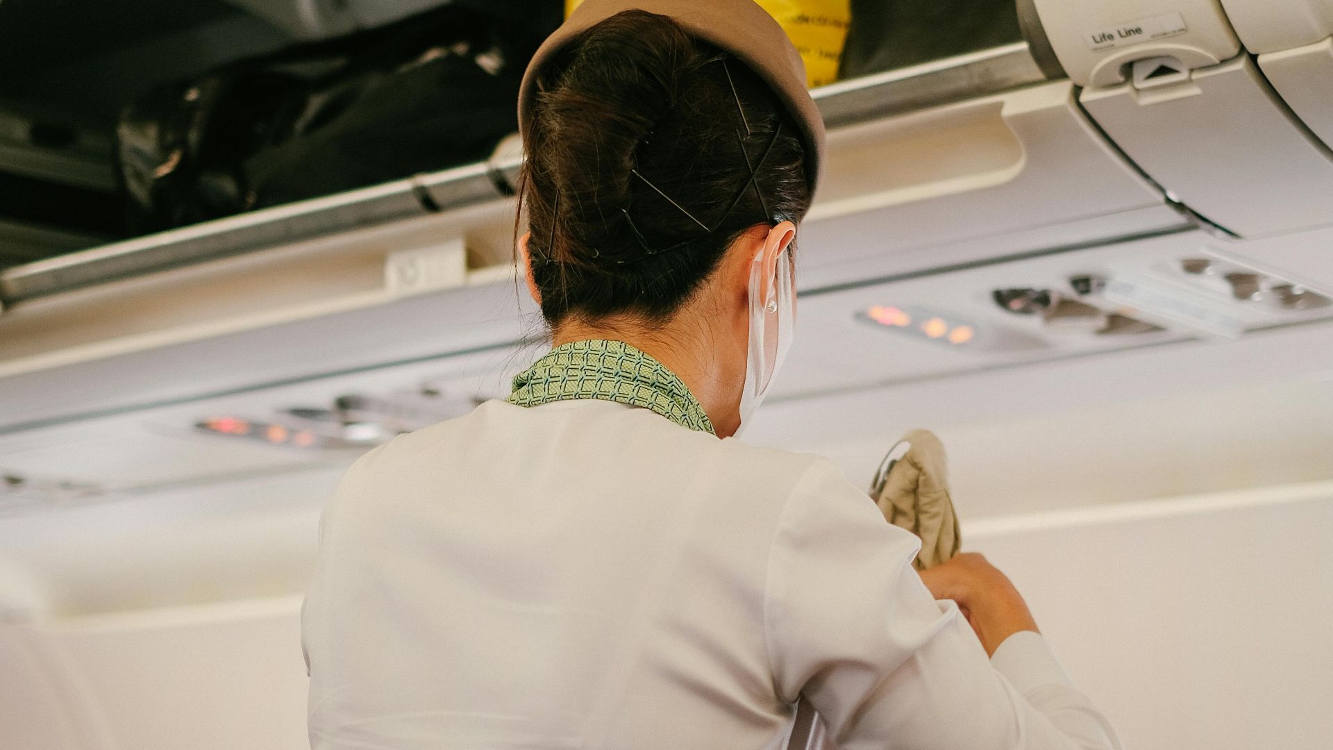 A flight attendant assists passengers with luggage in an airplane cabin.
