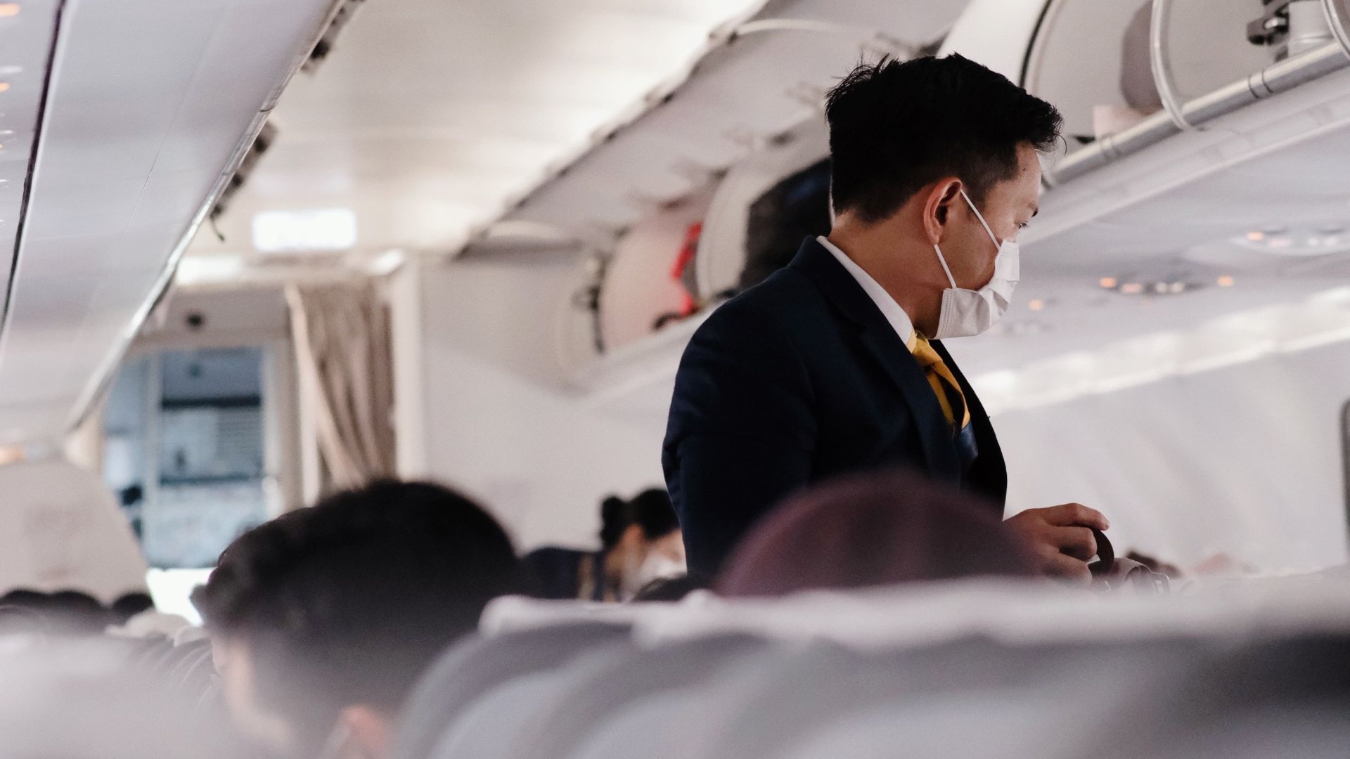 A flight attendant wearing a mask assists passengers on a commercial flight.