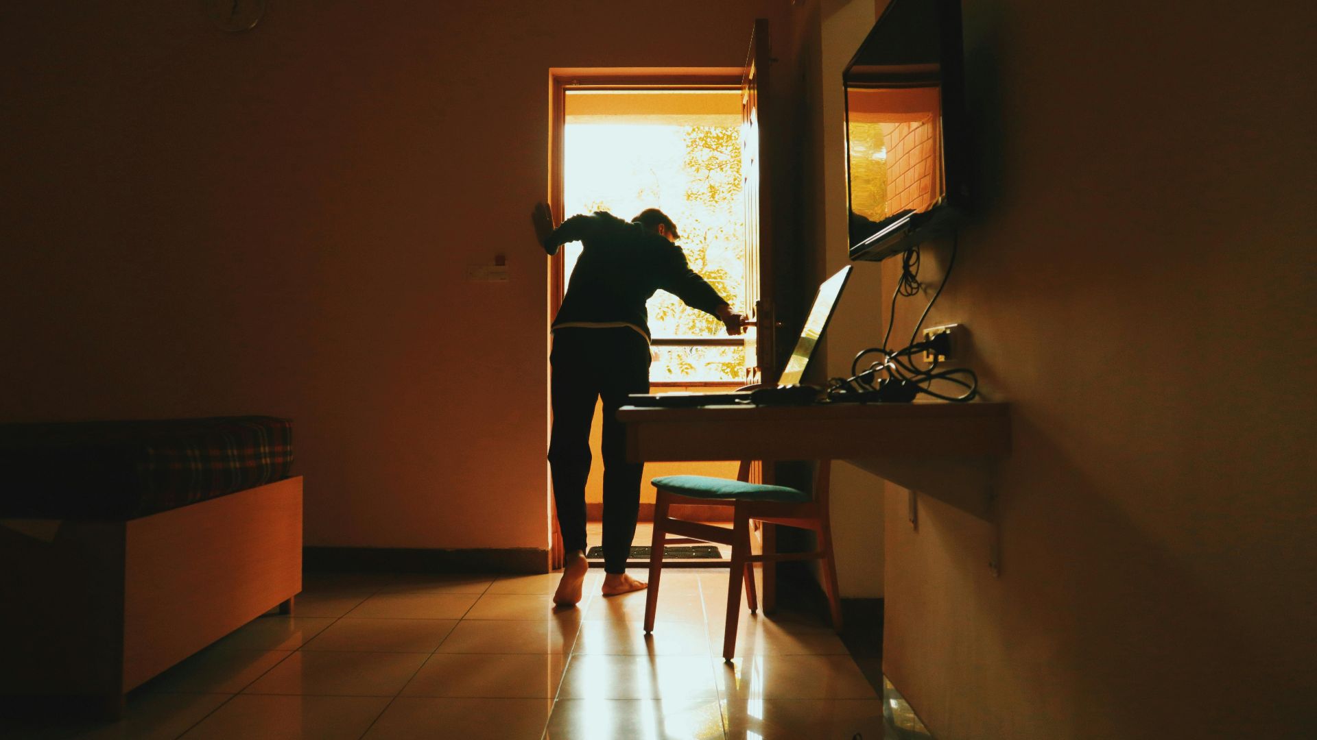 A silhouetted woman stands near a sunlit door in a modern interior, creating a warm ambiance.