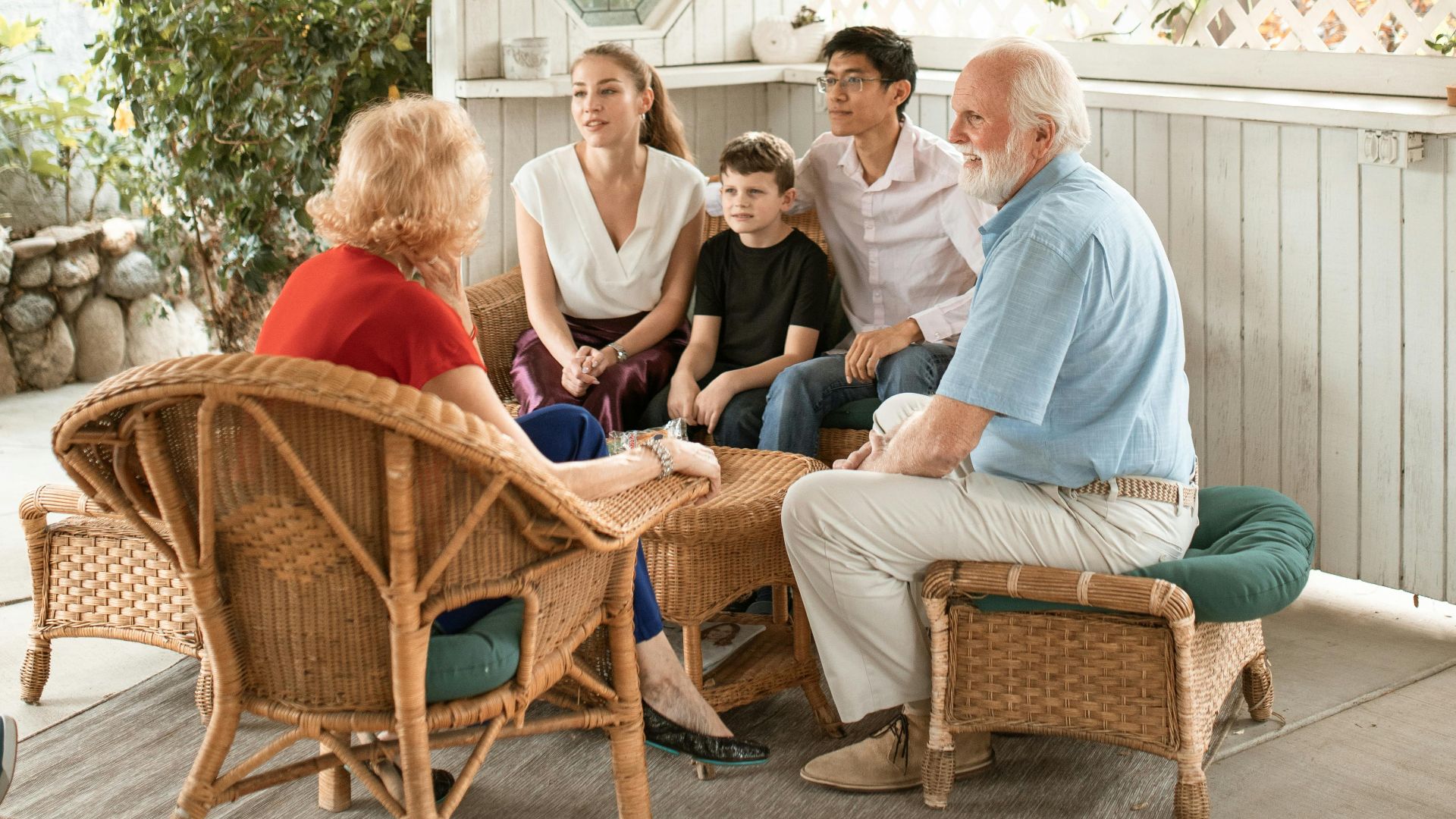 Family enjoys quality time together on cozy outdoor porch with wicker chairs.
