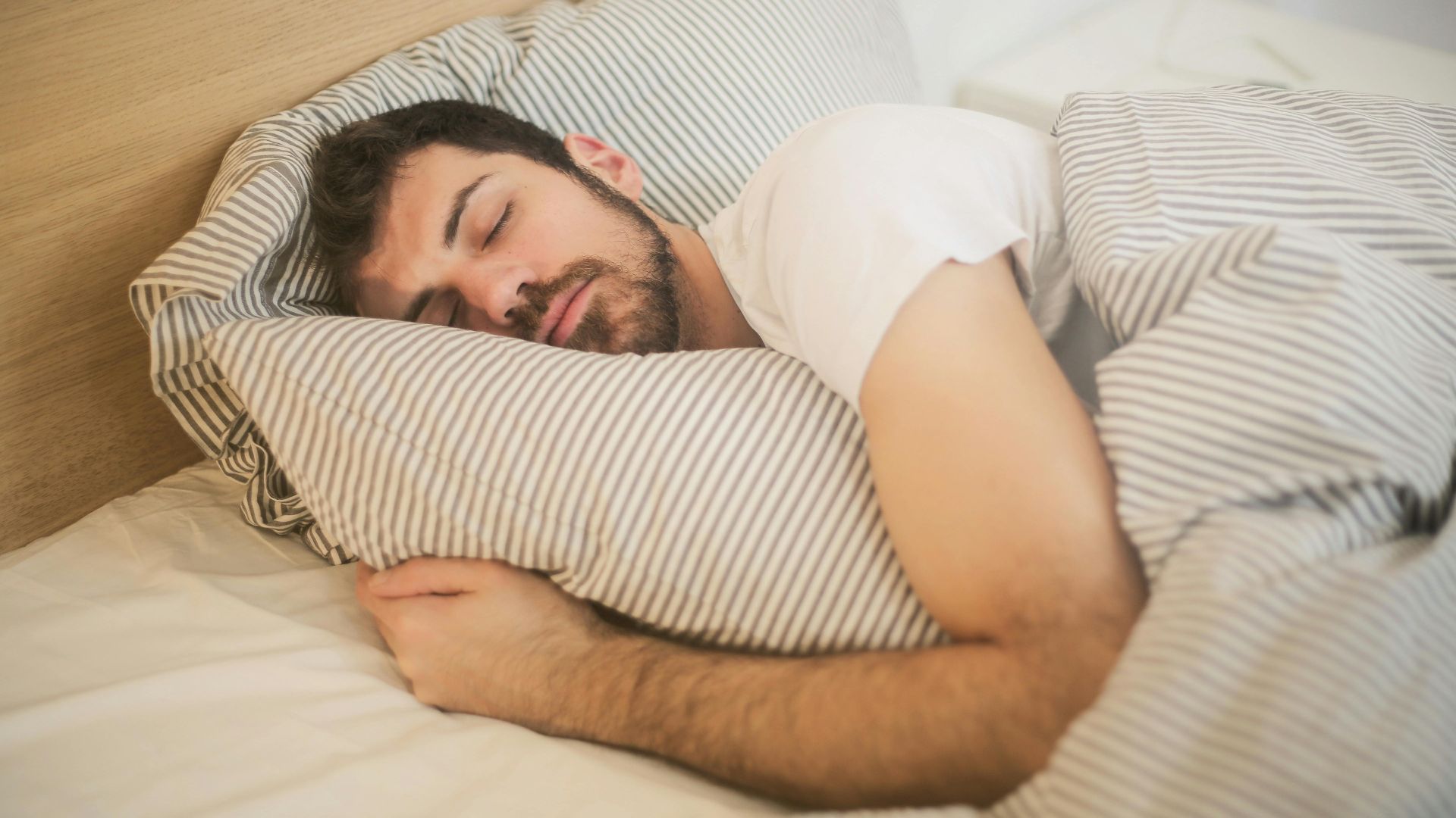 Man sleeping peacefully on striped bedding, embracing relaxation and comfort.