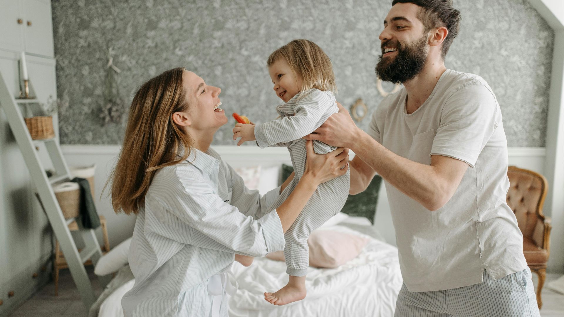 Smiling parents play with their young daughter in a bright, cozy bedroom, creating joyful family memories.