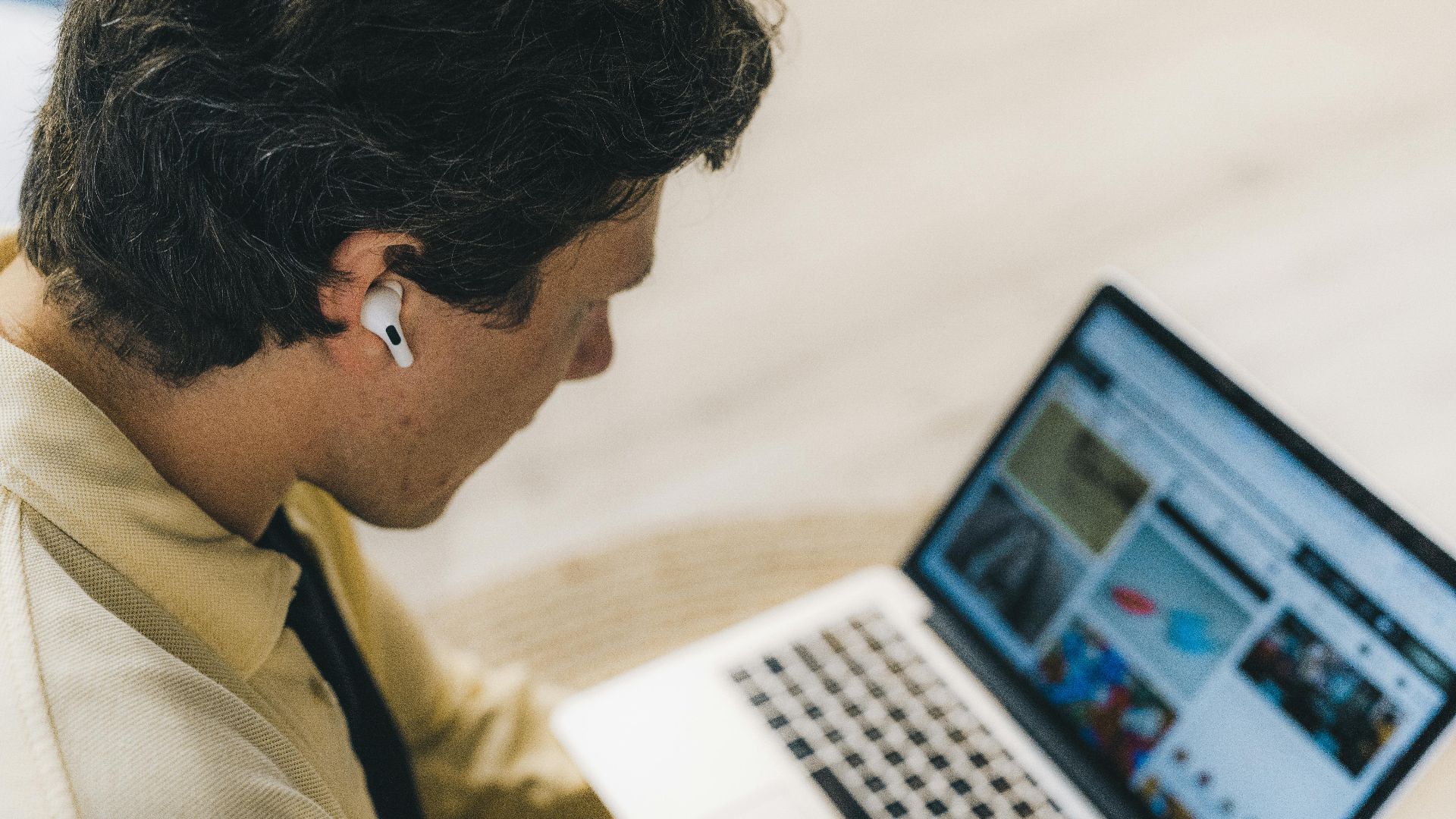 Man with earbuds working remotely on a laptop, embodying the digital nomad lifestyle, indoors.