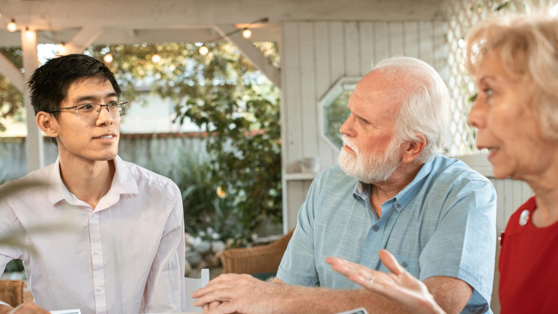 Senior couple and family member discussing ultrasound photos at an outdoor table.