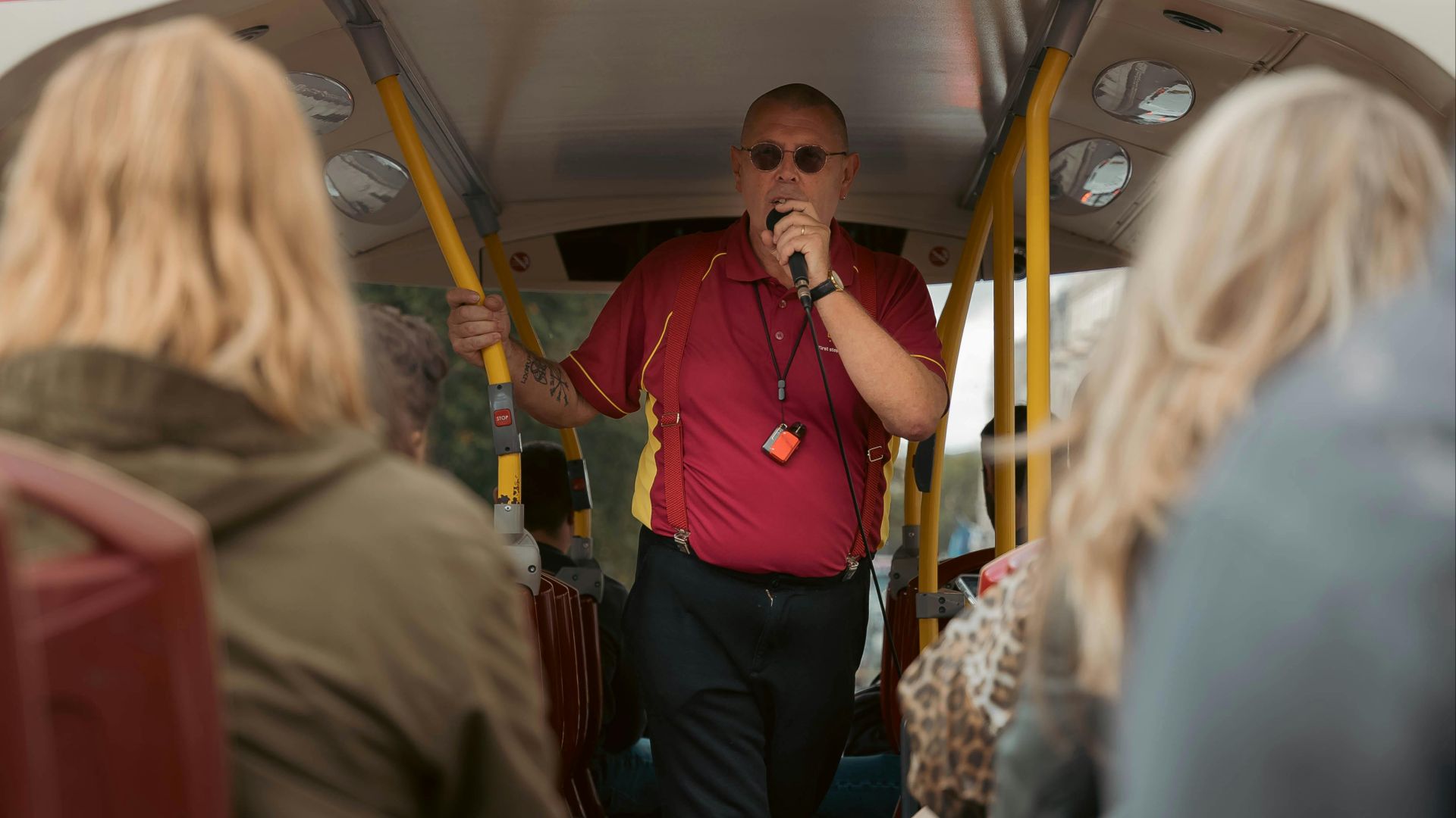 Tour guide engaging visitors on an open-top bus tour in London, UK.
