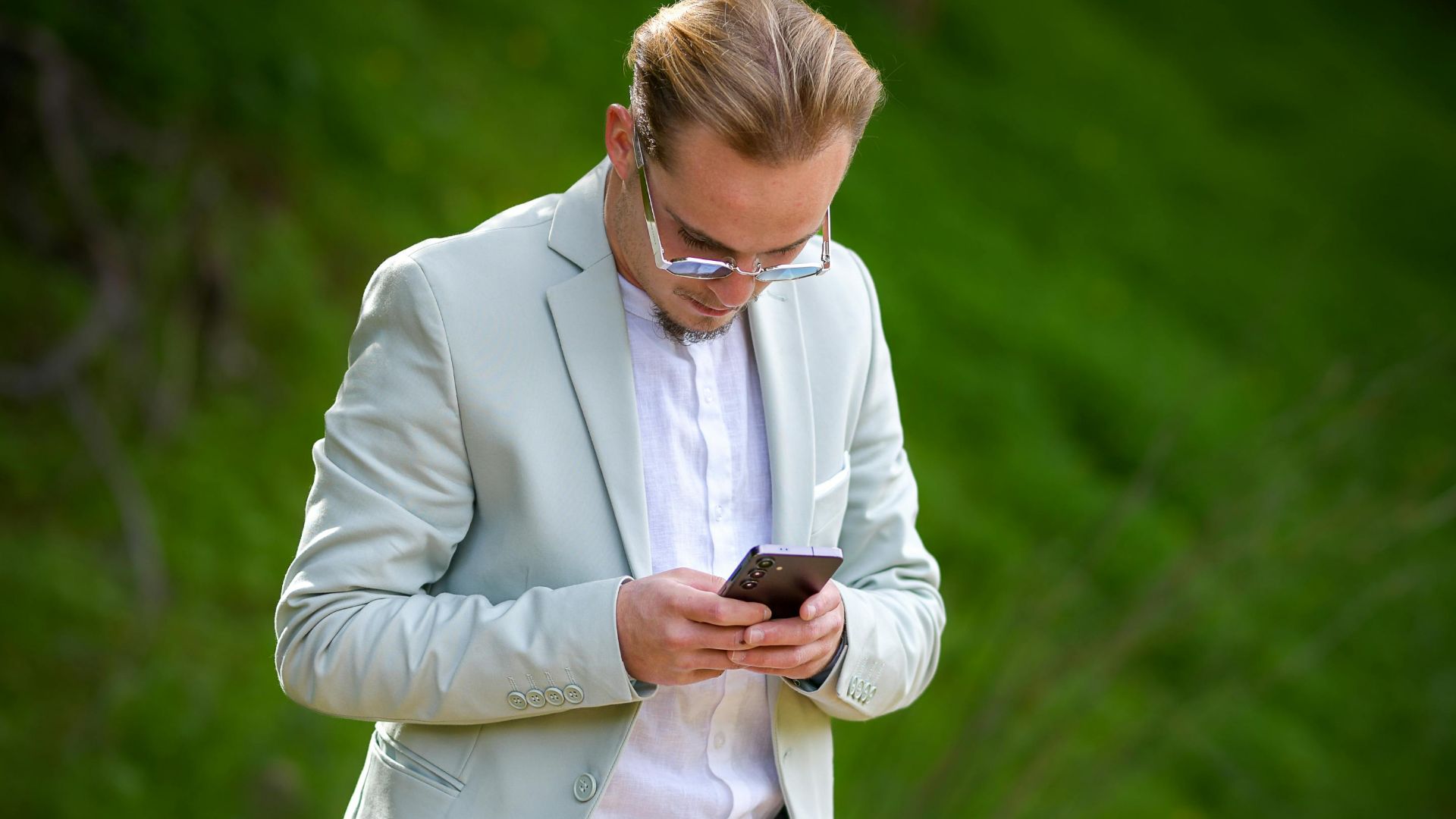 Man in a mint green suit engaging with his smartphone outdoors, showcasing modern lifestyle and fashion.