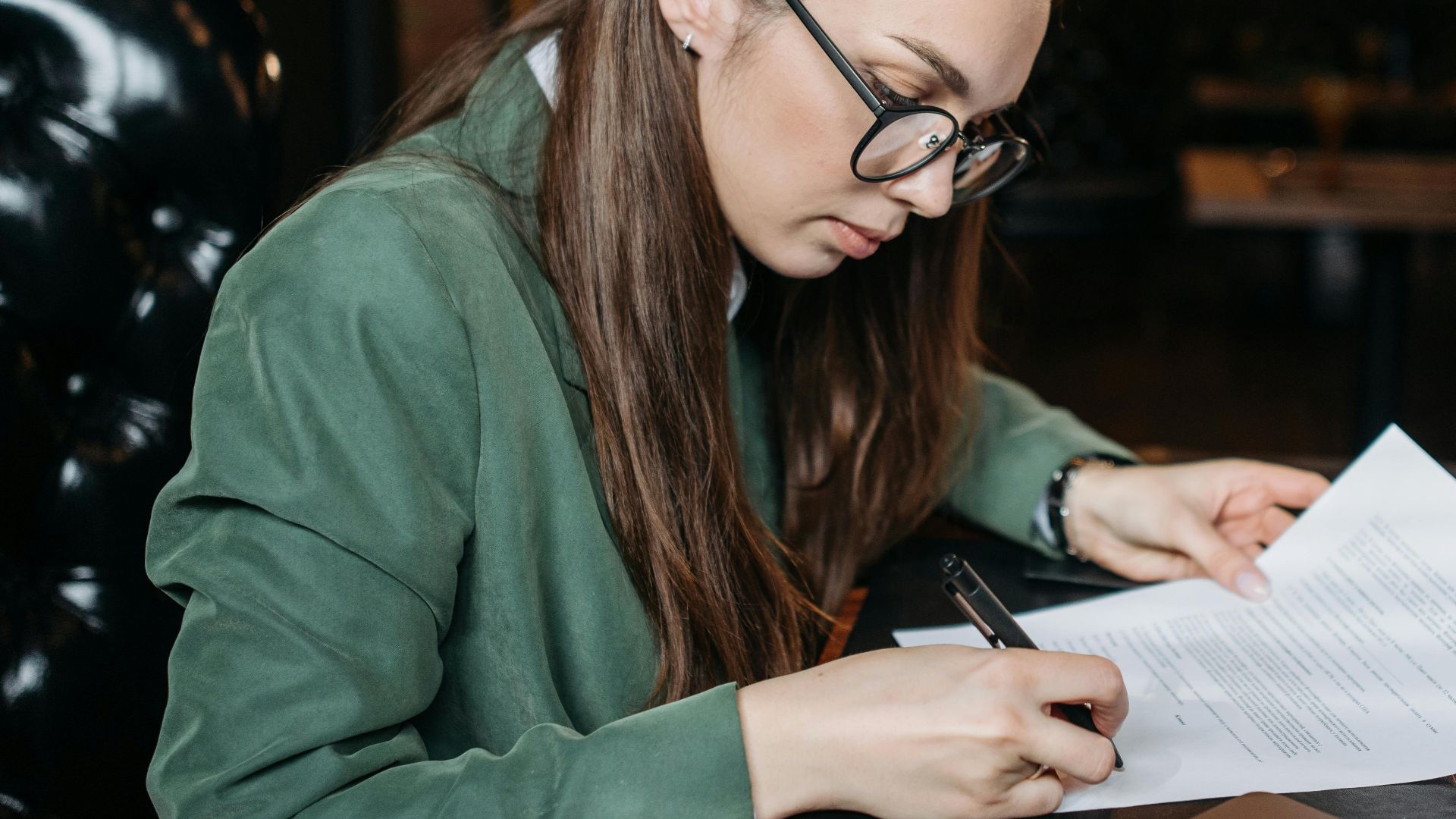 Focused businesswoman in green attire signing important documents at her desk.