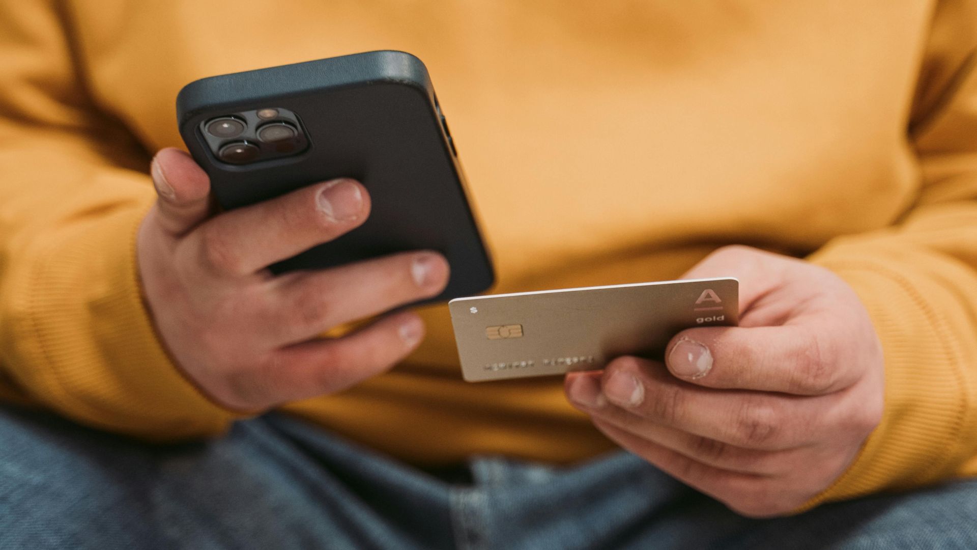 A man in casual attire using a smartphone and credit card indoors, focusing on online shopping.