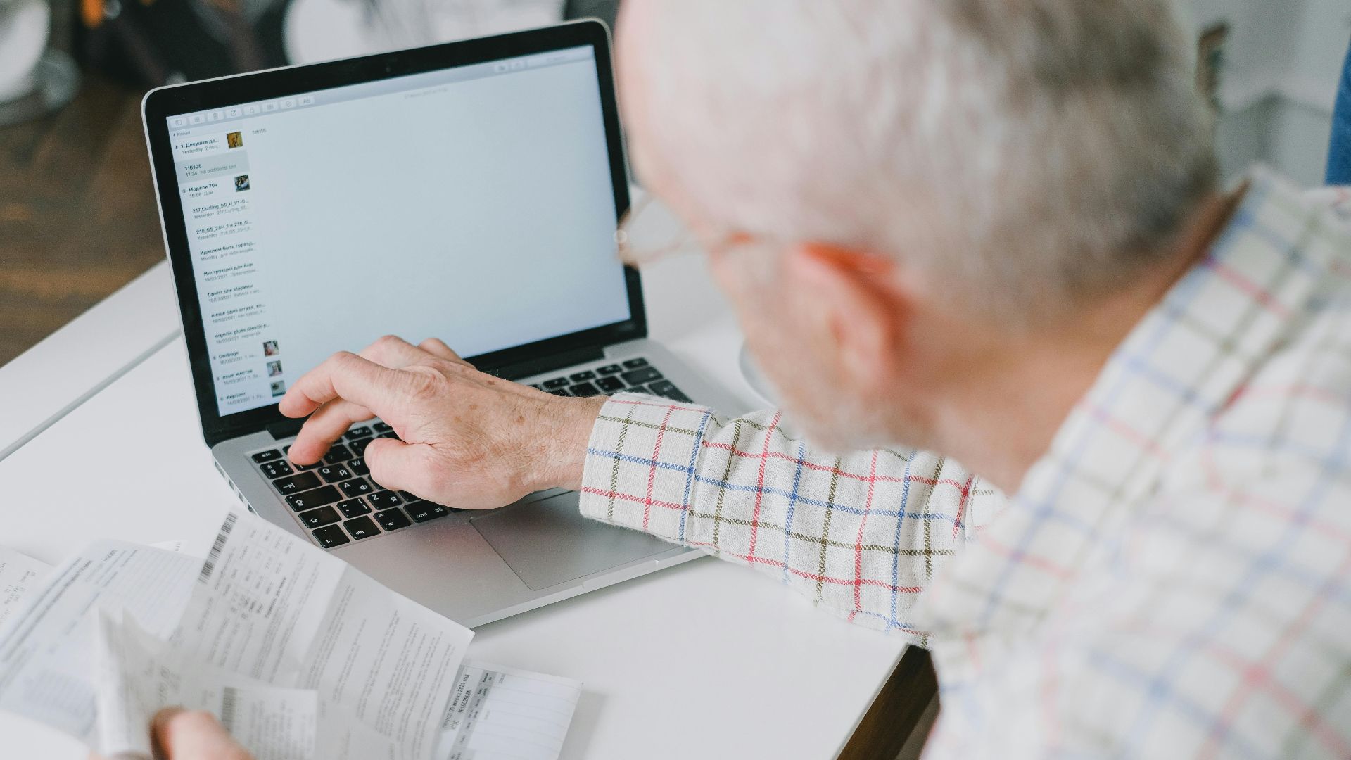 Elderly man at desk handling finances online with documents and laptop.