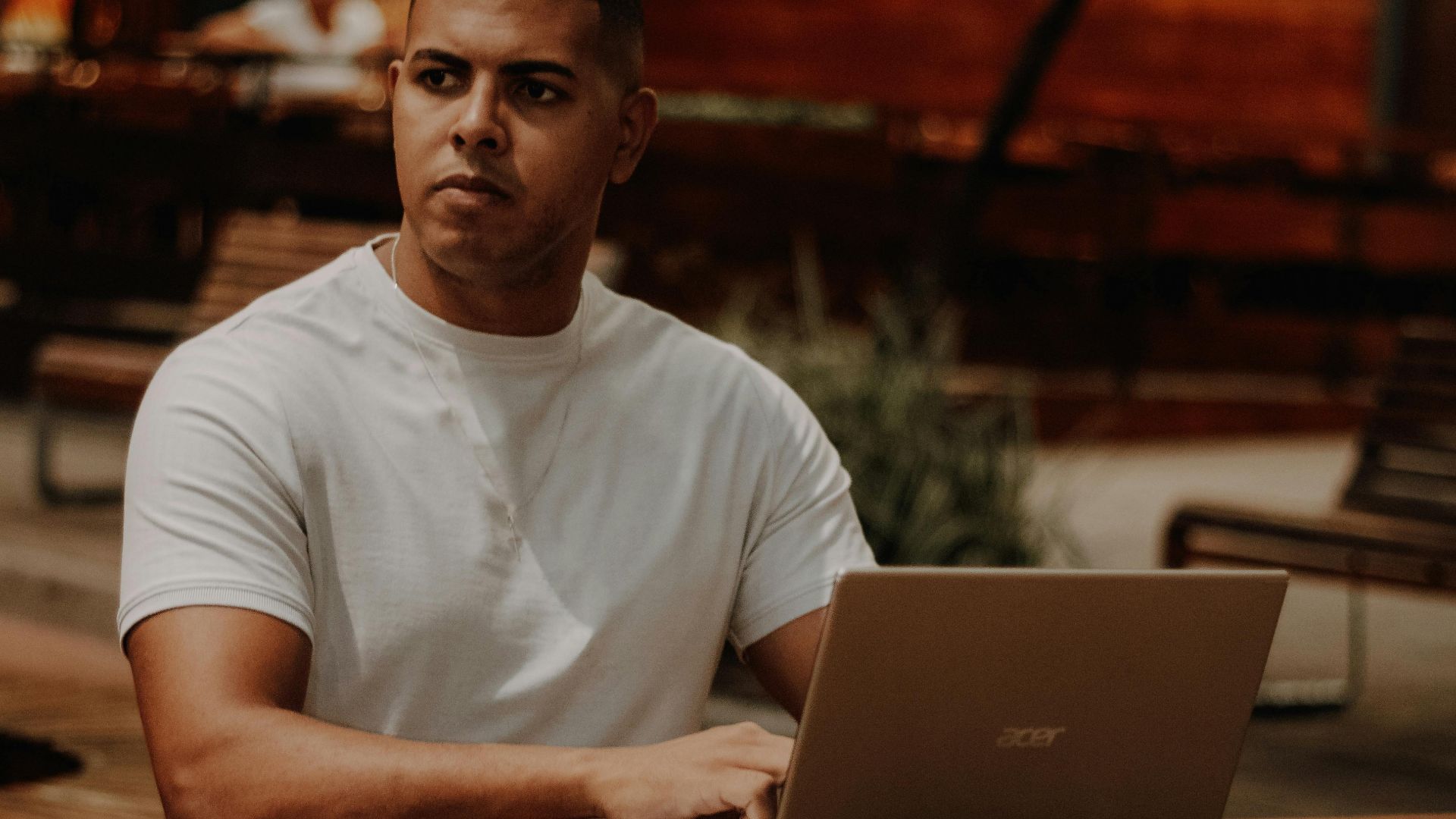 Man in white sitting at café outdoors with laptop, focused on work in Nova Iguaçu, Brazil.