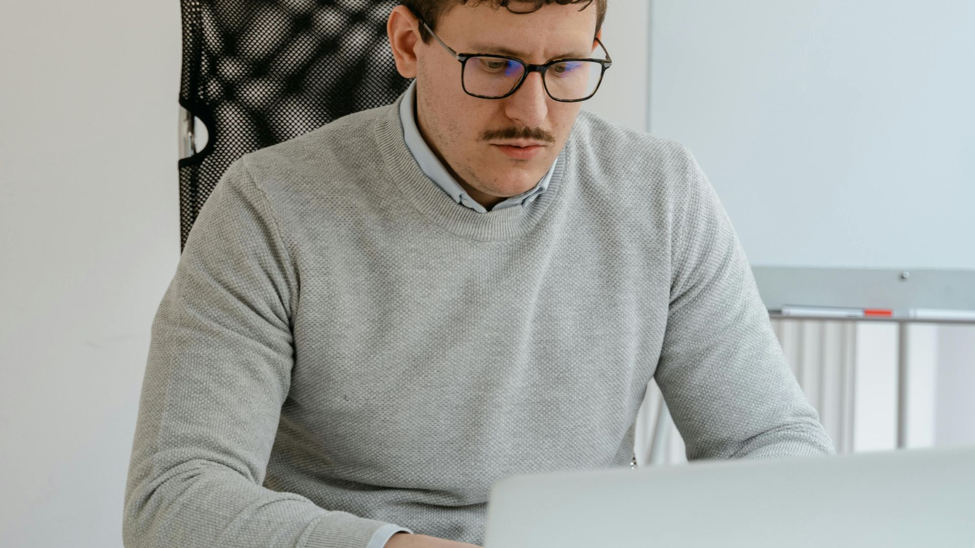 Businessman wearing eyeglasses working on a laptop in a modern office setting.