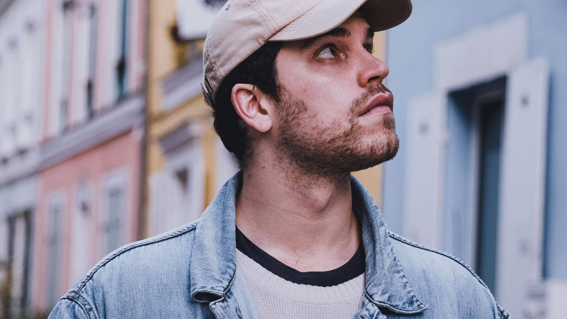 Portrait of a man in a denim jacket and cap looking around a colorful Parisian neighborhood.