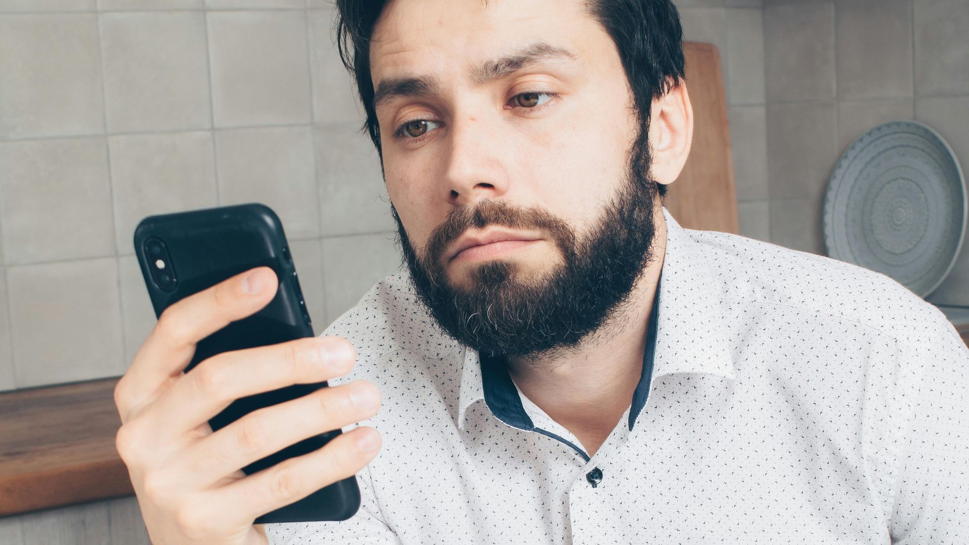 A man looks frustrated while checking his smartphone, possibly experiencing a banking issue or scam.