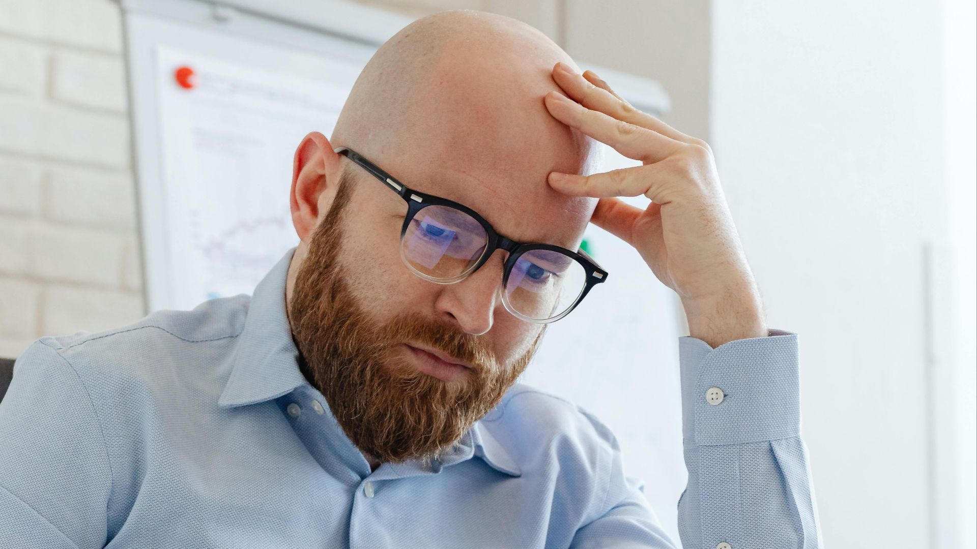 Caucasian businessman with beard and glasses reviewing documents in a modern office setting.