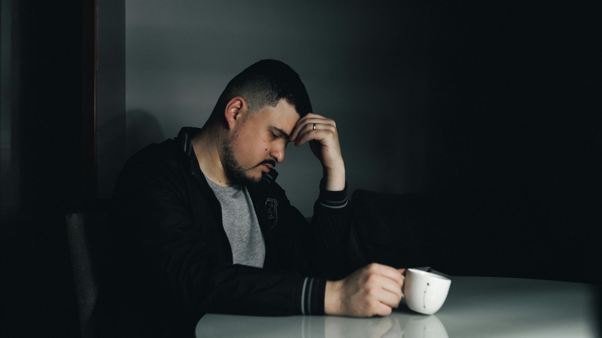 A thoughtful man in a dark room holding a coffee cup, depicting a moody morning scene.