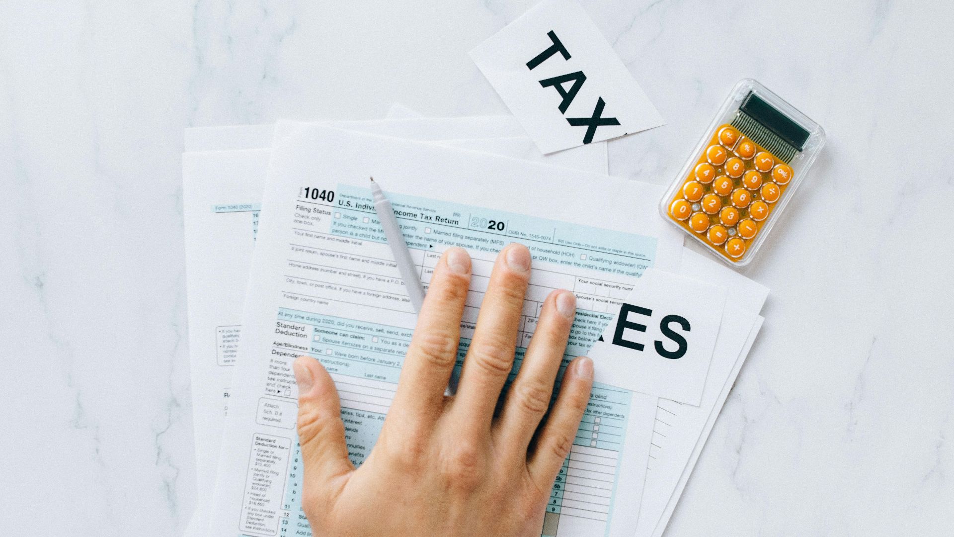 Close-up of a hand on tax form 1040 with a calculator on a desk.