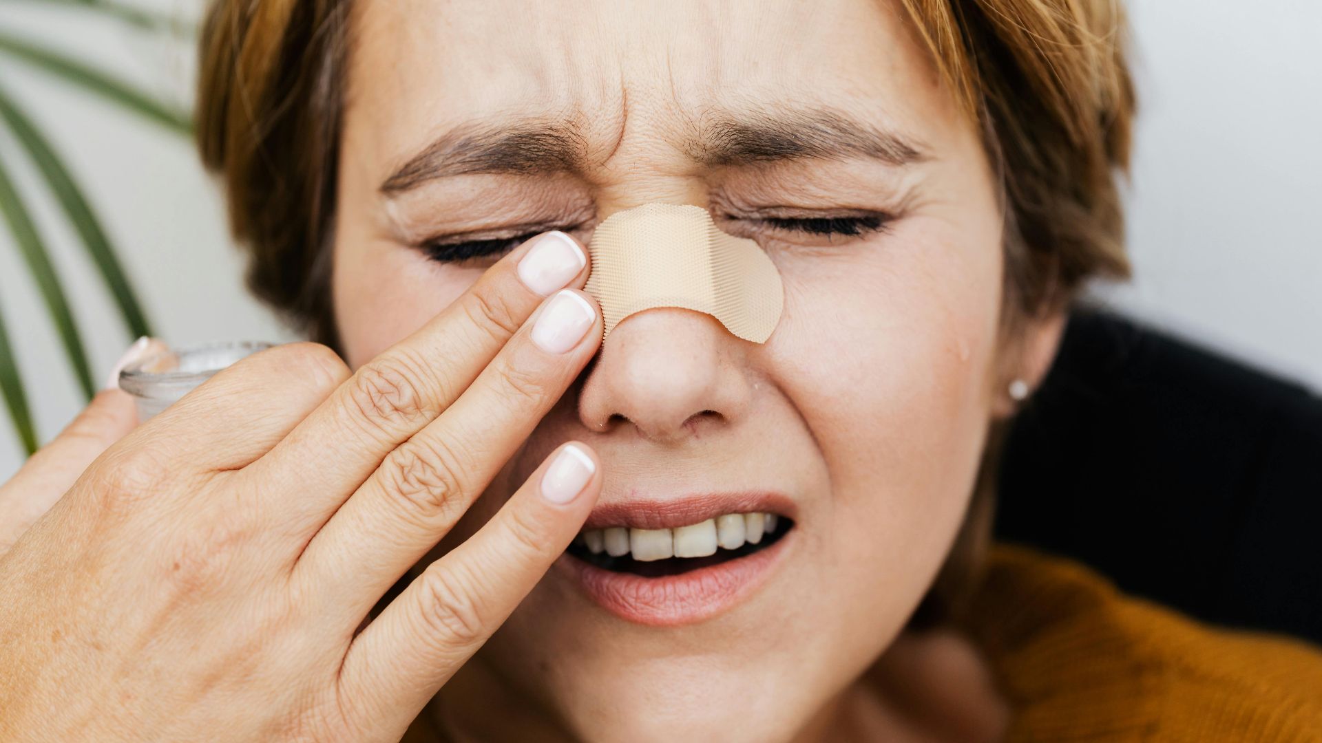 Close-up of a woman with a band aid on her nose, showing pain and discomfort.