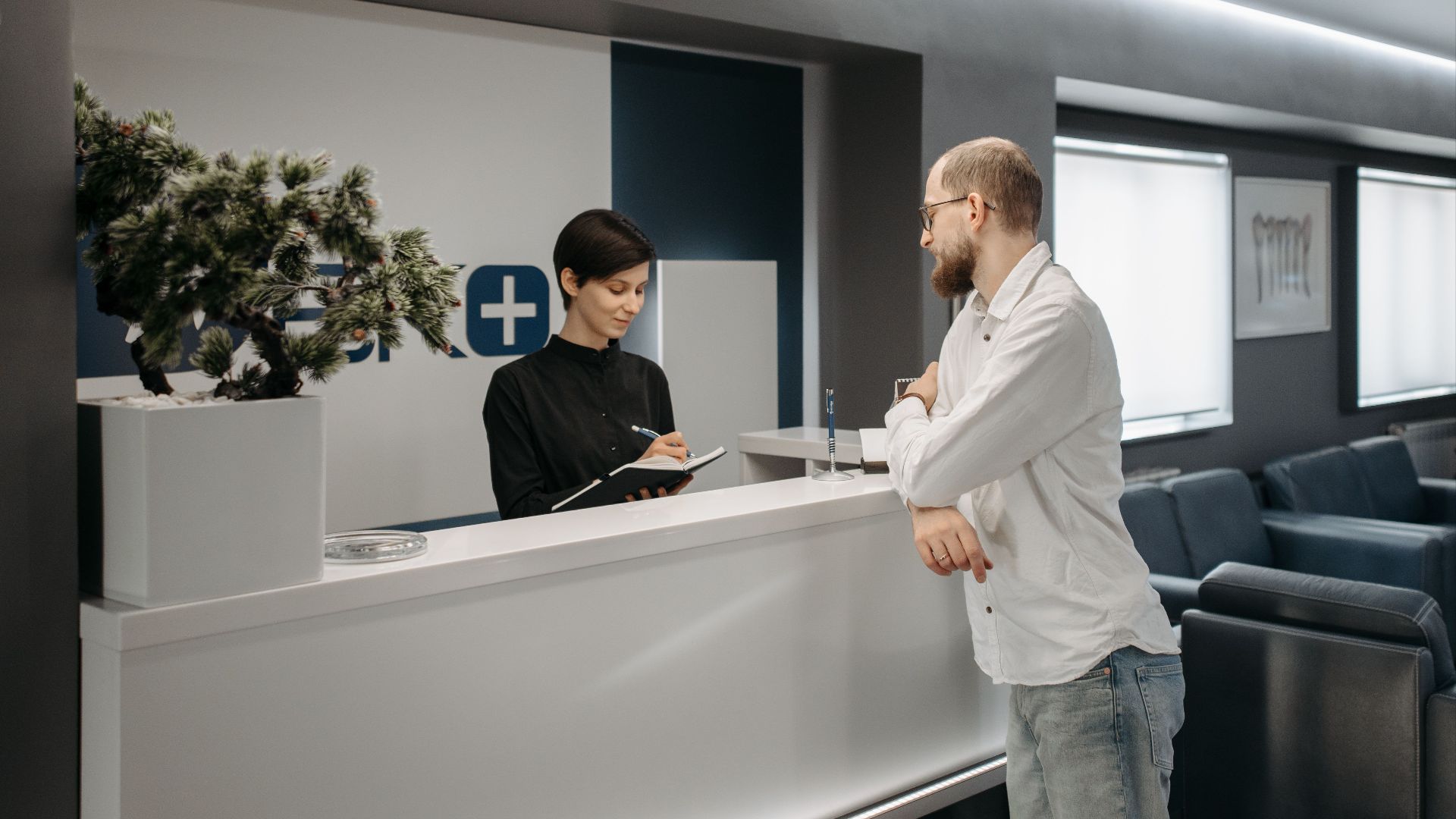 A man consults a receptionist in a modern clinic setting with contemporary design.