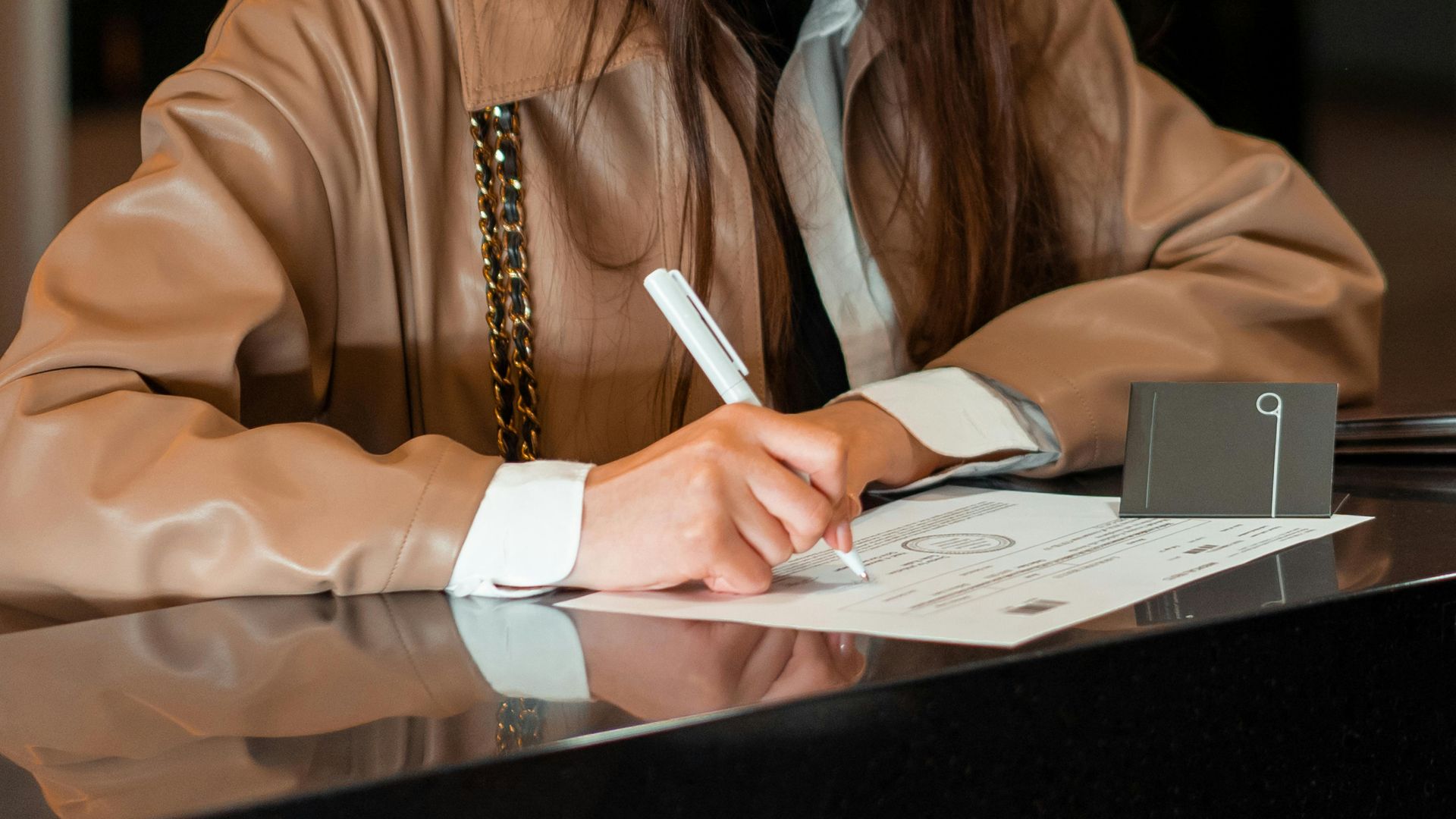 Close-up of a woman signing a document at a sleek reception counter, indoor setting.