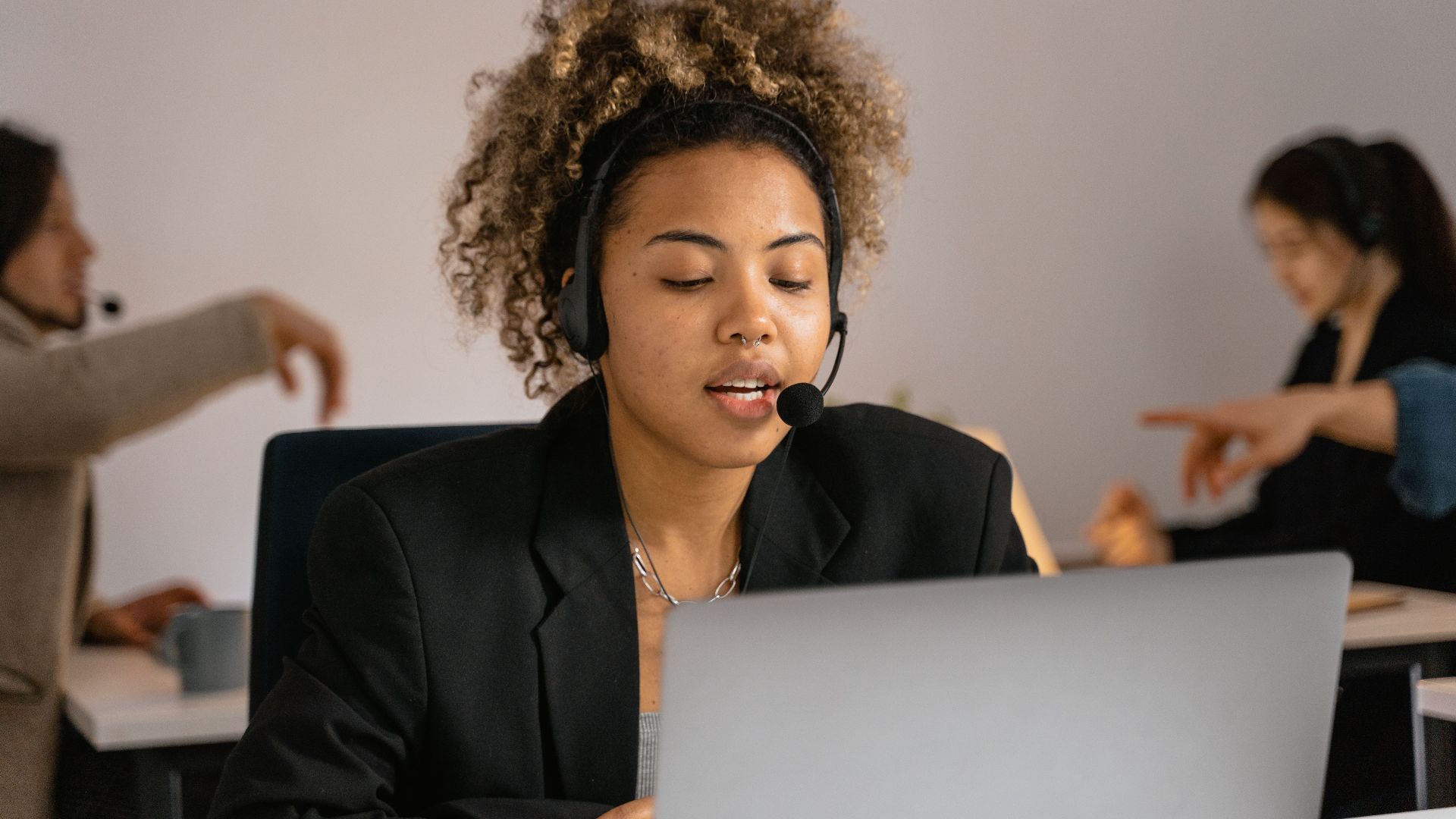 Customer support agent with headset working on laptop in office.