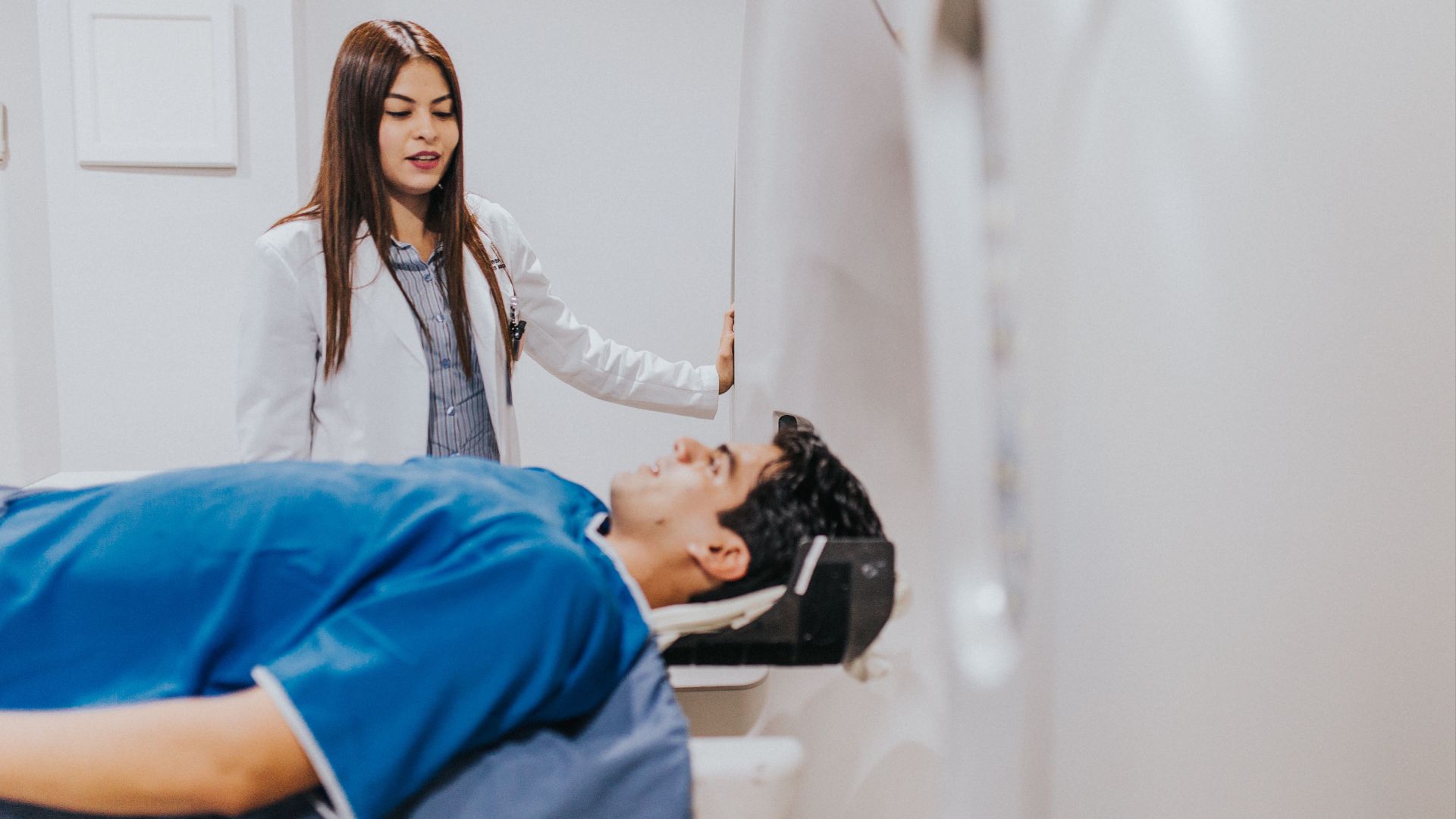 A doctor stands beside a patient in an MRI room, ensuring a smooth examination process.