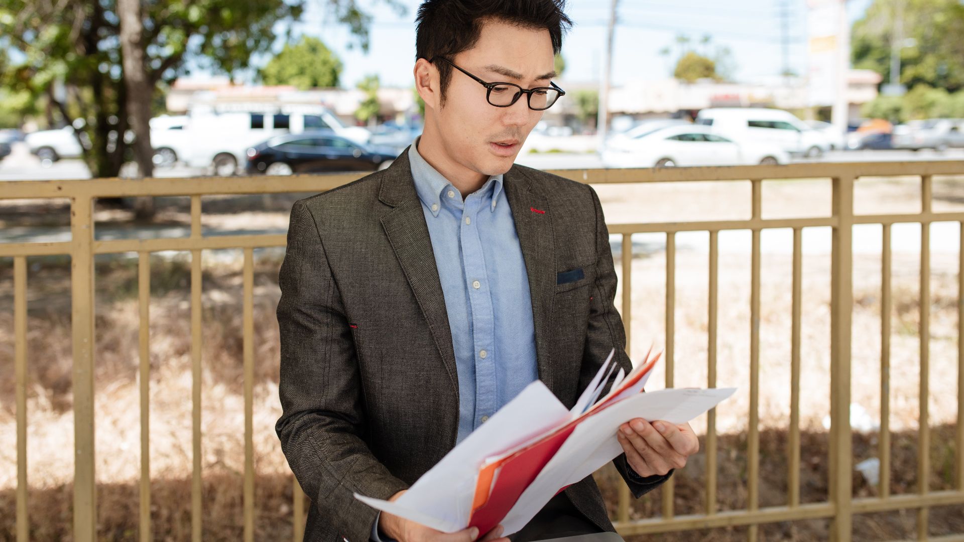 Asian businessman in a suit checking documents outdoors on a sunny day.