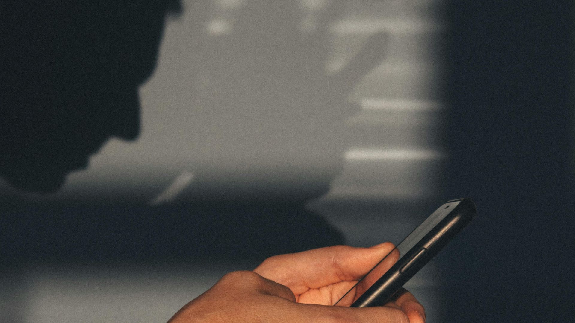 A man wearing a bracelet holds a smartphone with shadows and reflections visible.