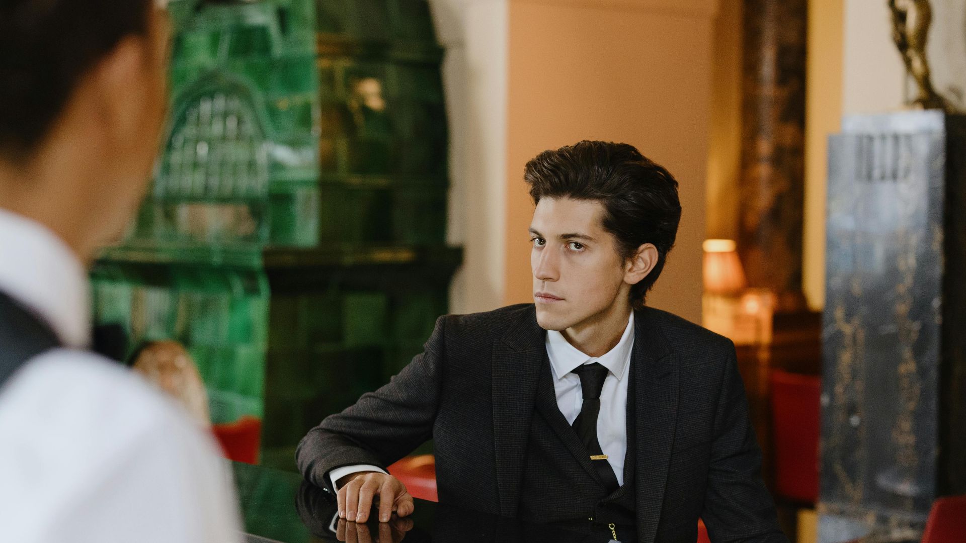 Sophisticated man in a suit sitting at a vintage bar counter indoors, exuding elegance and style.