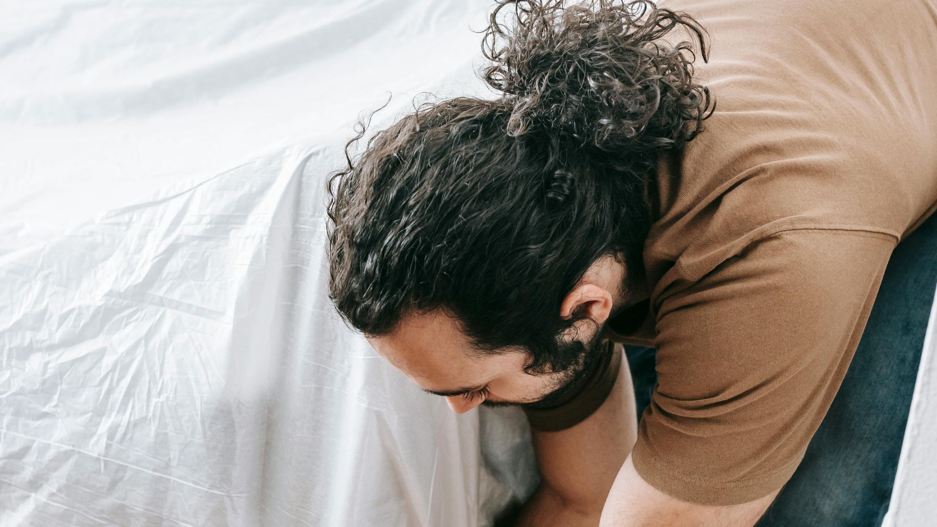A man carefully covers a sofa with a white cloth for protection or relocation.