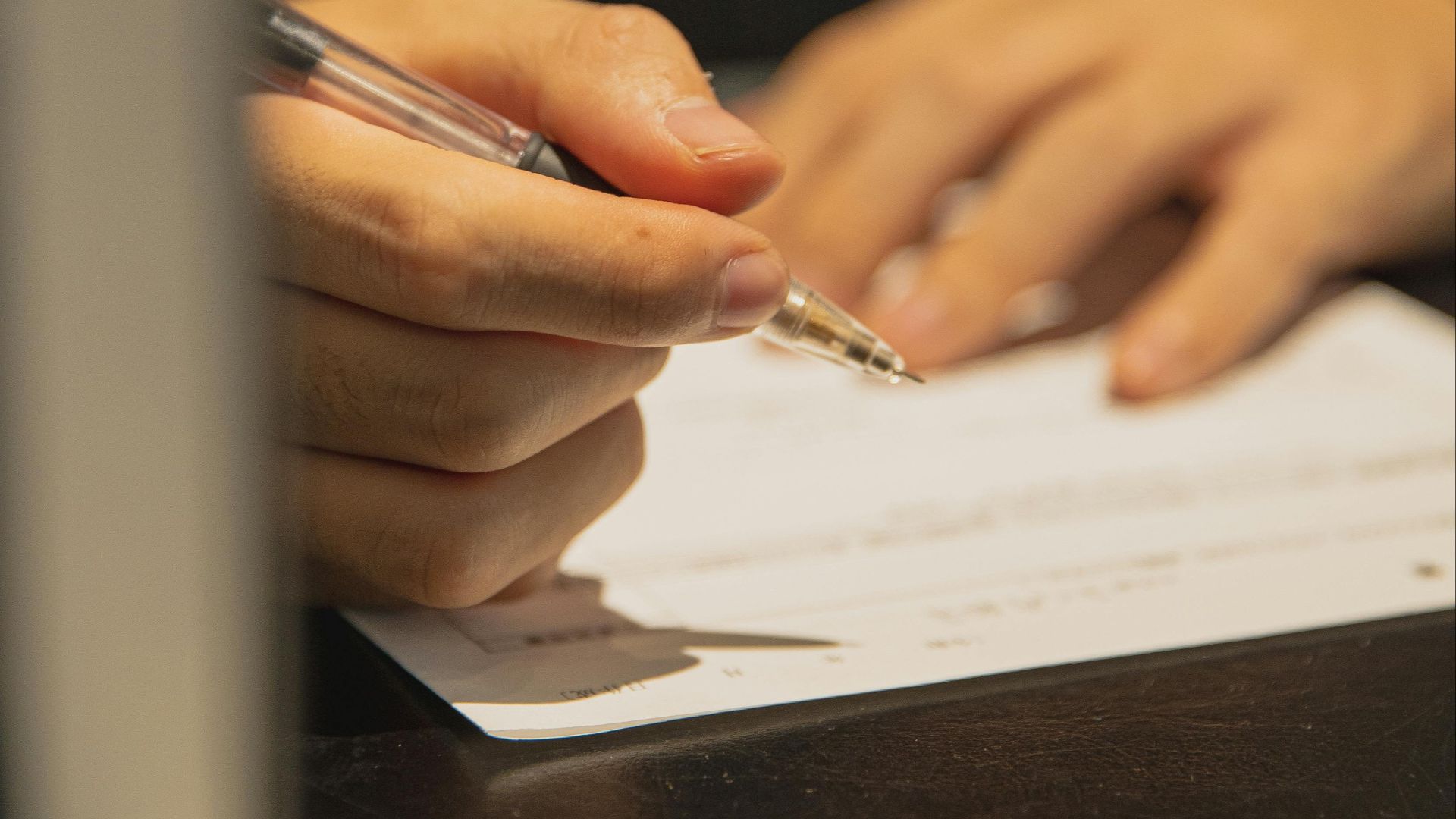 Crop anonymous male with pen in hand and paper on table filling in document