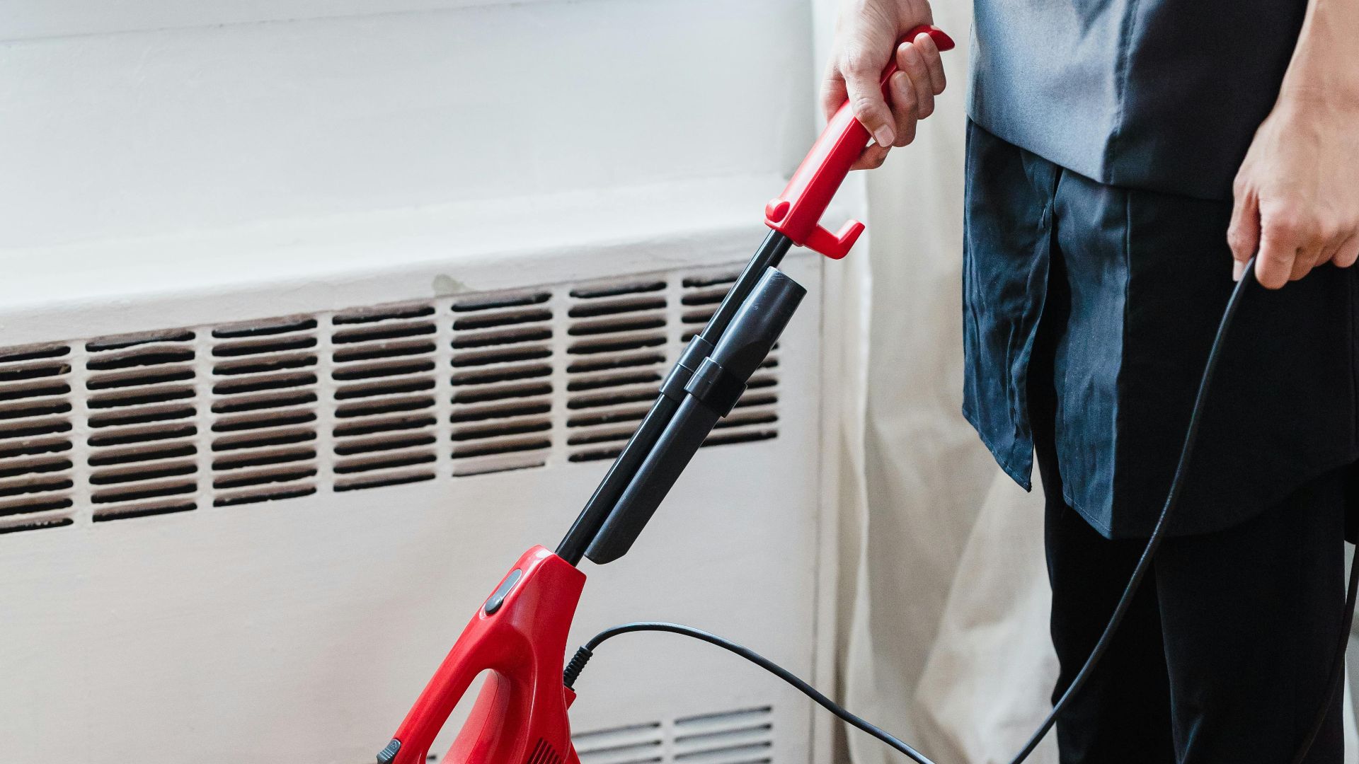 Person cleaning wooden floor with red vacuum cleaner in a well-lit room.